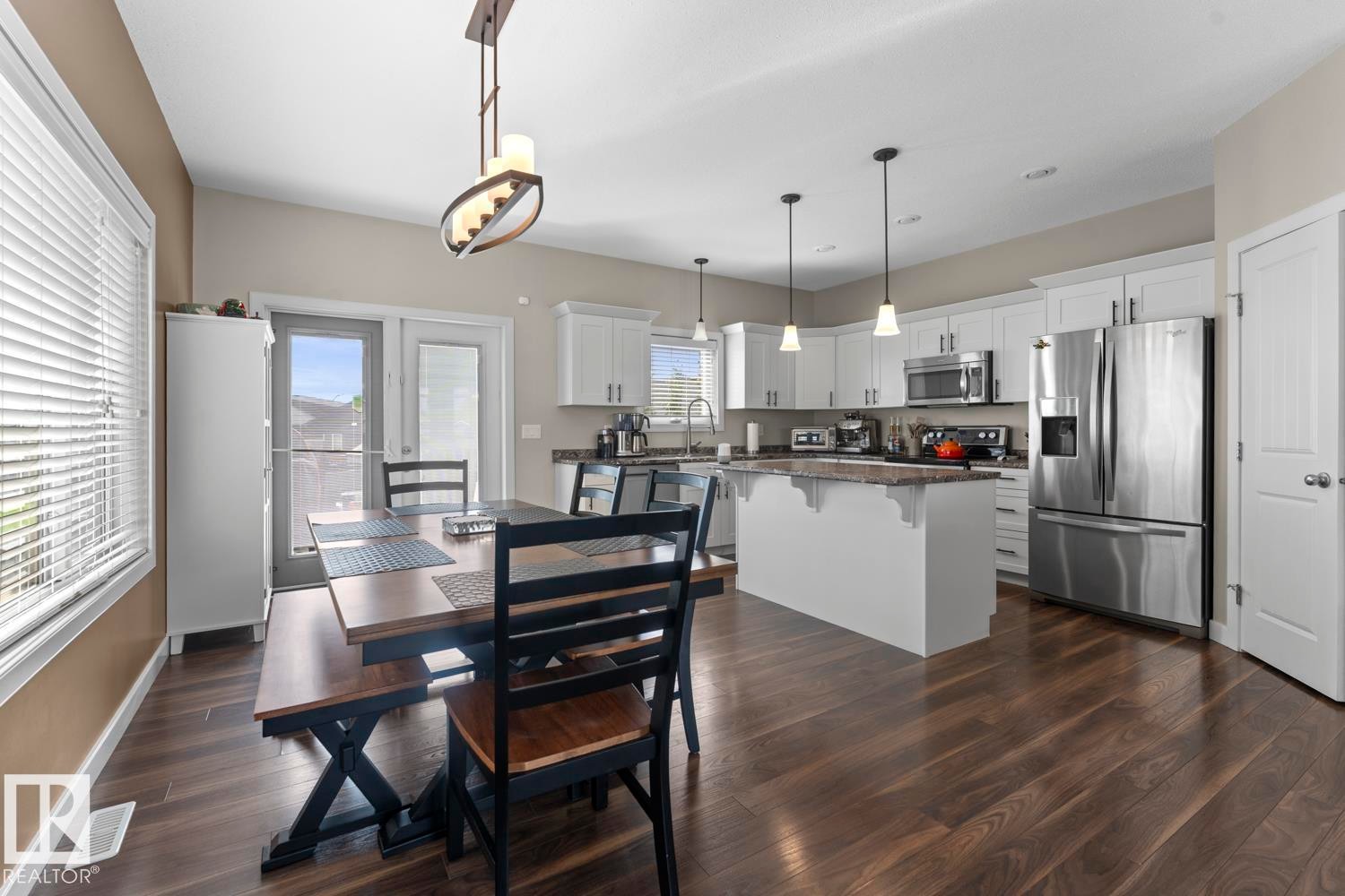 Kitchen and dining area featuring wood-finish flooring, white cabinetry, stainless steel appliances, a kitchen island, and a glass-paneled door - 35 Falcon Road, Cold Lake, AB