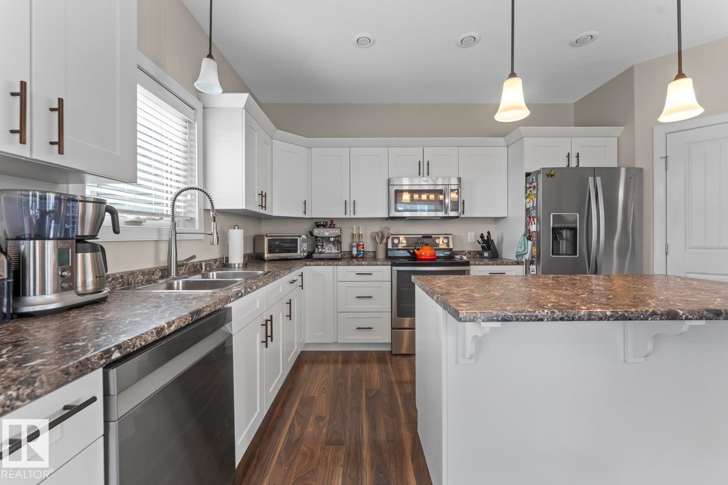Kitchen featuring white cabinetry, dark wood-finish flooring, a central island with a stone-look countertop, stainless steel appliances, and pendant lighting - 35 Falcon Road, Cold Lake, AB