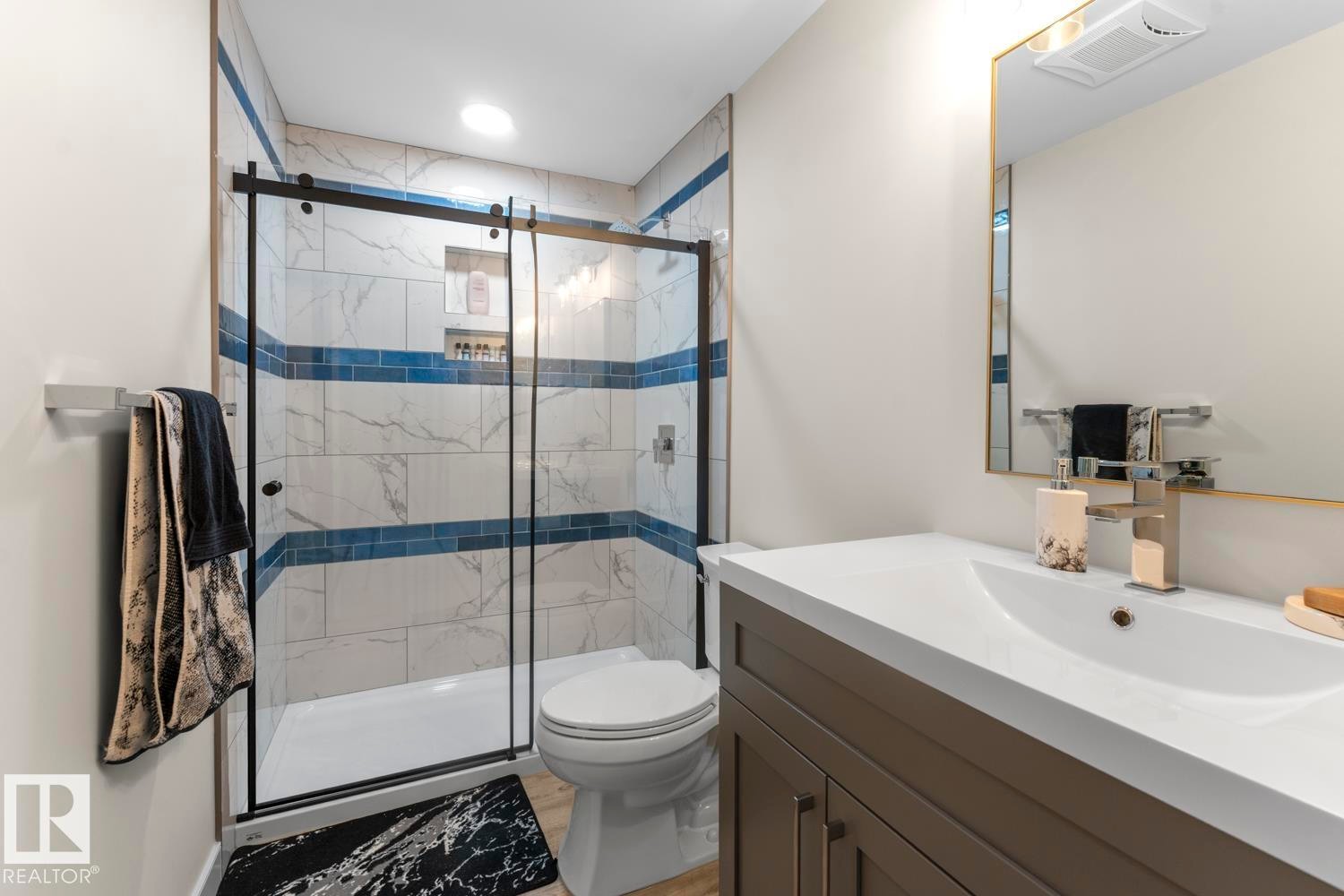 Bathroom featuring a glass-enclosed shower with a black frame, subway tile with blue accent bands, and a recessed shower niche - 35 Falcon Road, Cold Lake, AB