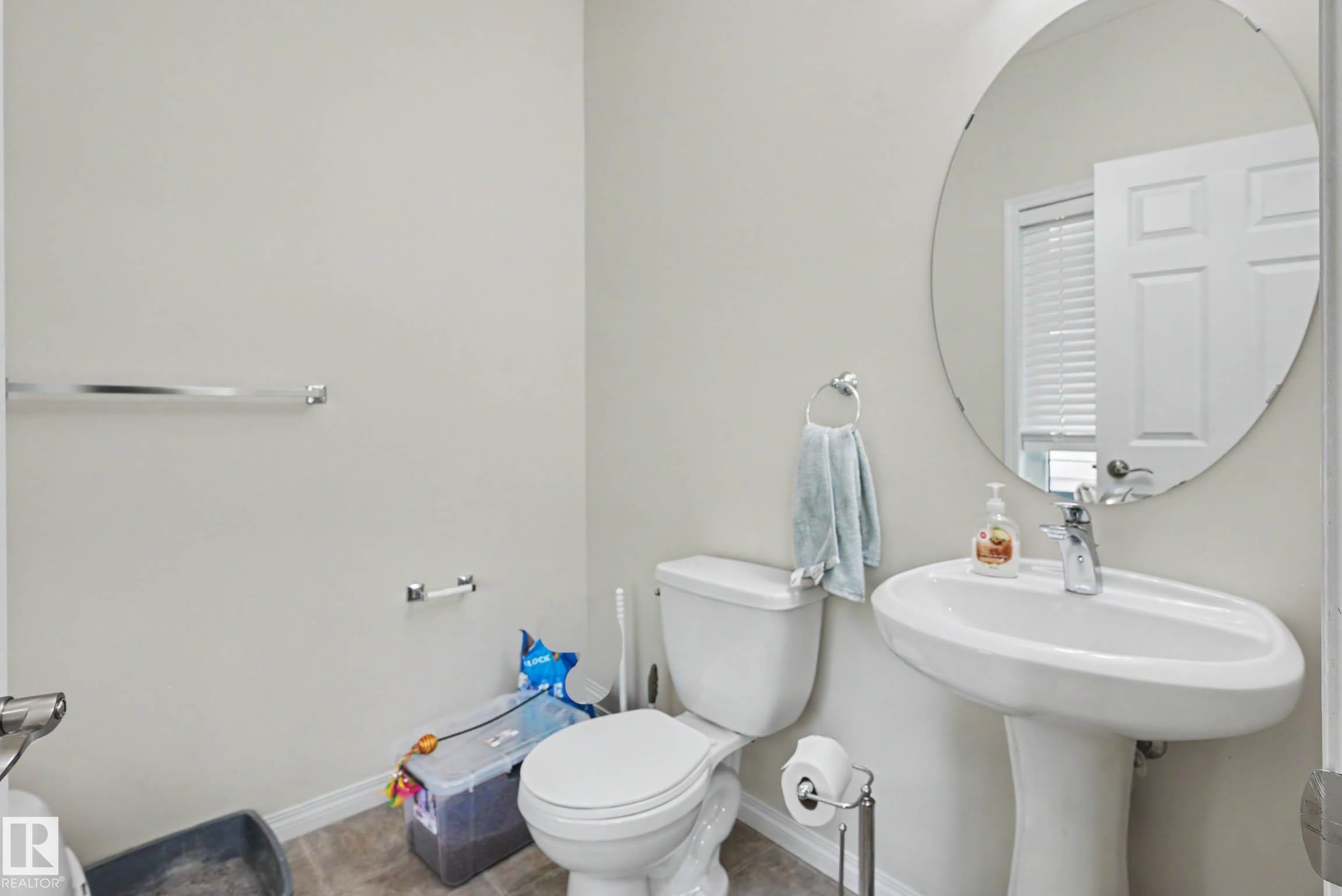 Powder room featuring a pedestal sink with a single-handle faucet, a circular mirror, and tile flooring - 2007 72 Street, Edmonton, AB - Indoor Photo Showing Bathroom