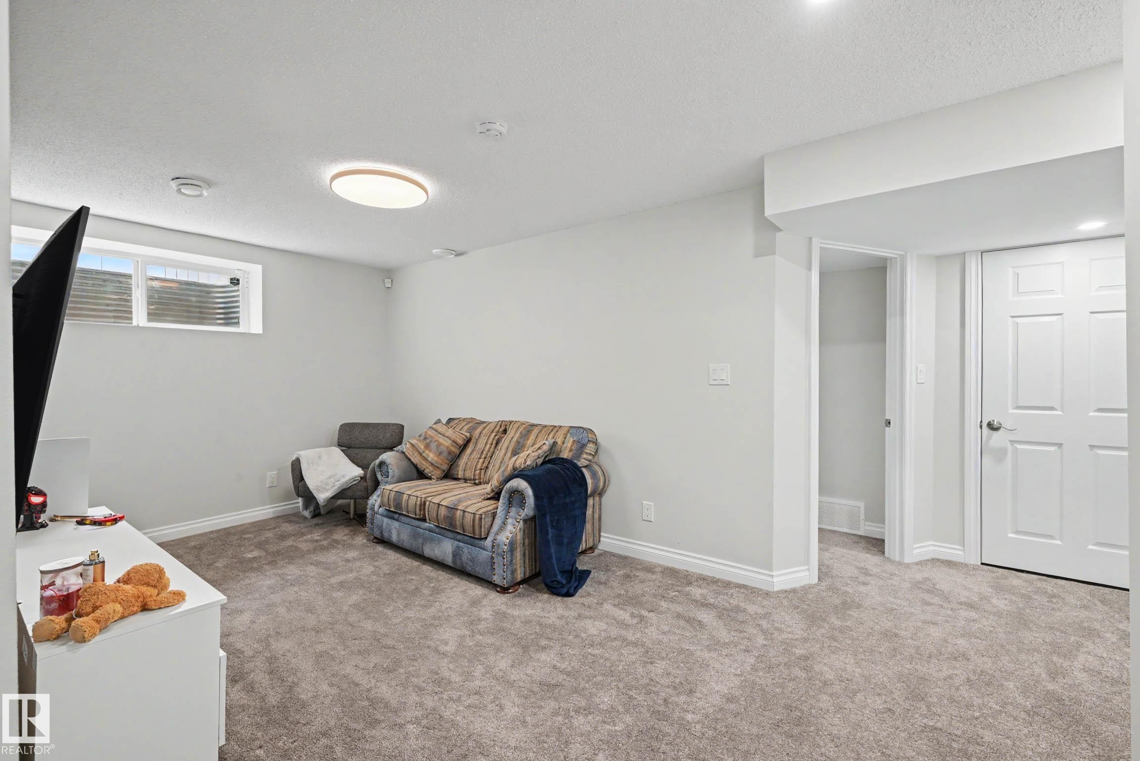 Spacious room featuring light gray wall paint, gray carpet flooring, white baseboards, and a white ceiling with a modern flush-mount light fixture - 2007 72 Street, Edmonton, AB - Indoor
