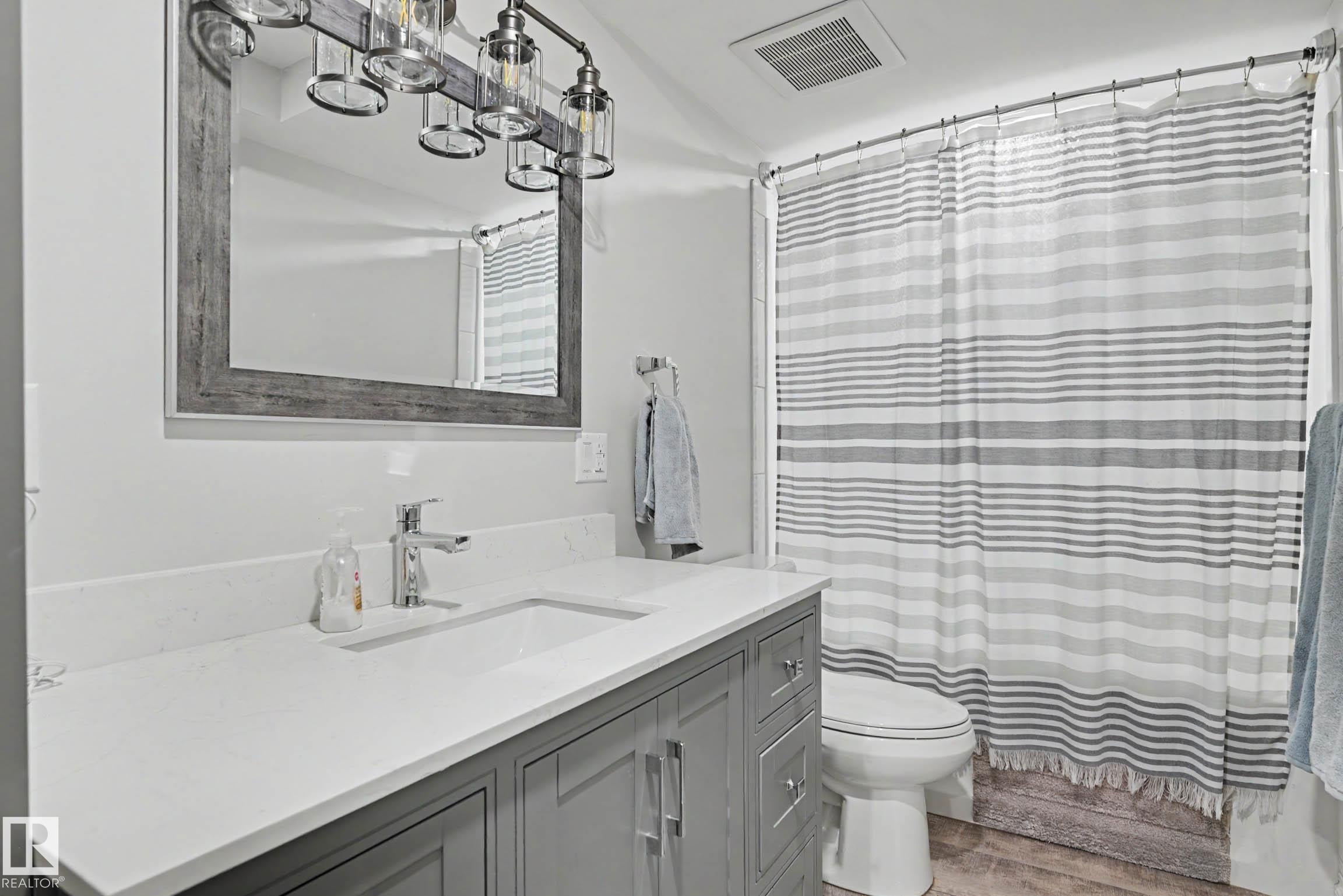 Bathroom featuring a gray vanity with a white countertop and integrated sink, chrome faucet, and a large mirror with a gray wood-look frame - 2007 72 Street, Edmonton, AB - Indoor Photo Showing Bathroom