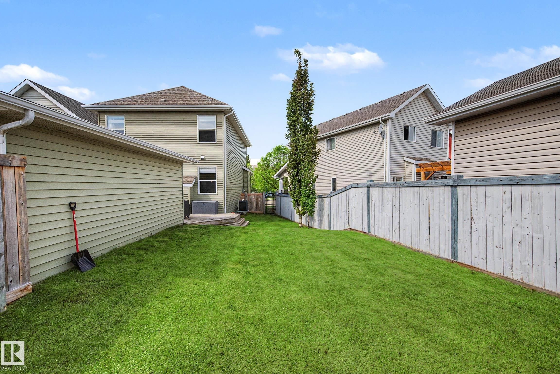 Expansive grassy backyard featuring a tall, slender tree, a wooden fence, and a multi-level deck - 2007 72 Street, Edmonton, AB - Outdoor With Exterior