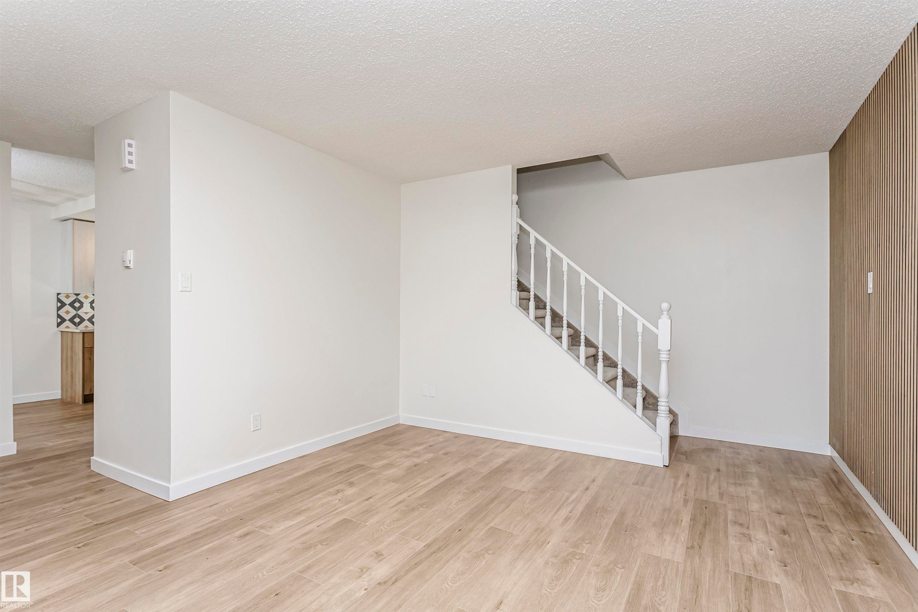 Open concept living area featuring light wood-finish flooring, white painted walls, a white staircase with balusters, and a textured accent wall - 5418 144B Avenue, Edmonton, AB