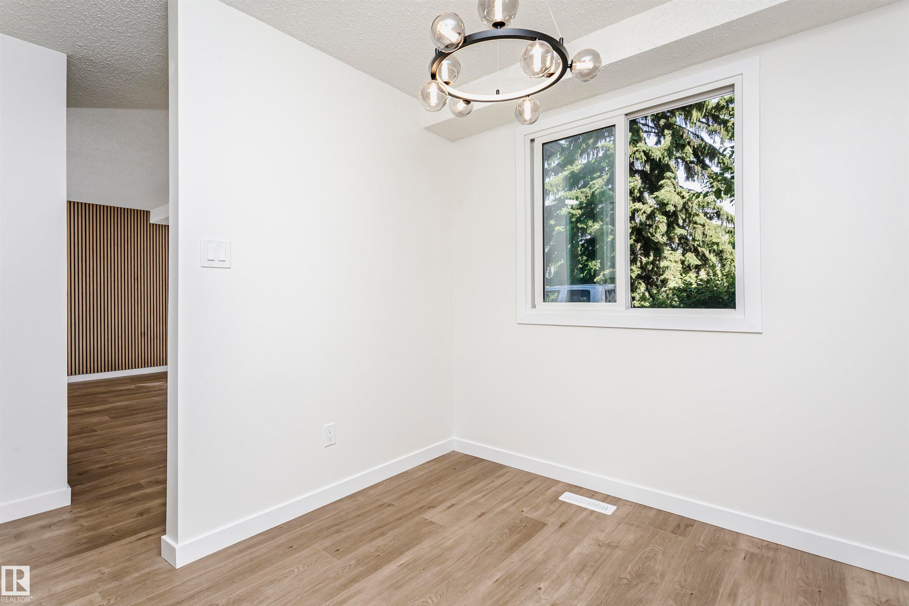 Room with light wood-finish flooring, white walls, and a modern circular chandelier - 5418 144B Avenue, Edmonton, AB