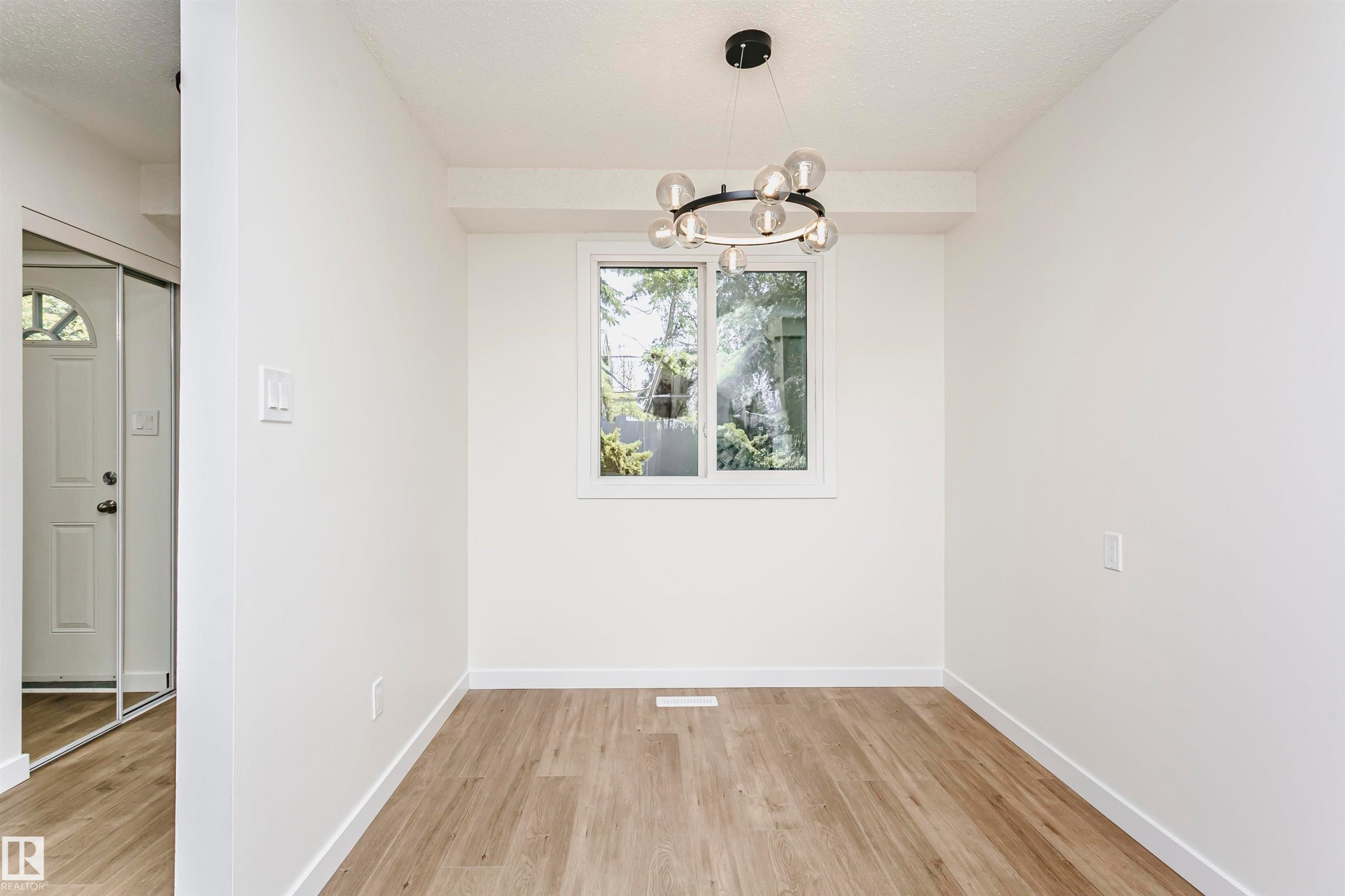 Light-filled interior space featuring a contemporary chandelier, a white-framed window, and wood-finish flooring - 5418 144B Avenue, Edmonton, AB
