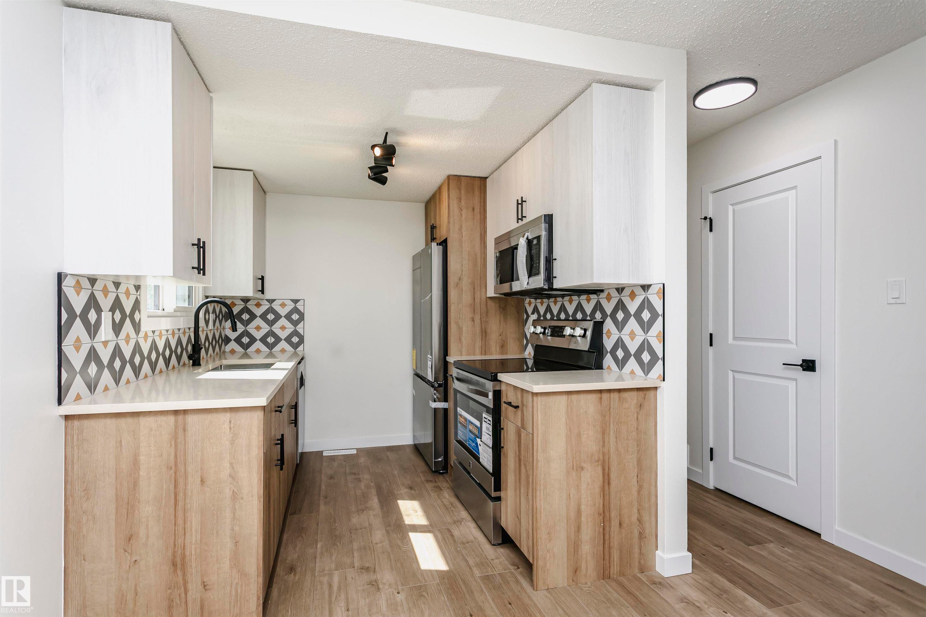 Contemporary kitchen featuring two-tone cabinetry, stainless steel appliances, a geometric tile backsplash, and wood-finish flooring - 5418 144B Avenue, Edmonton, AB