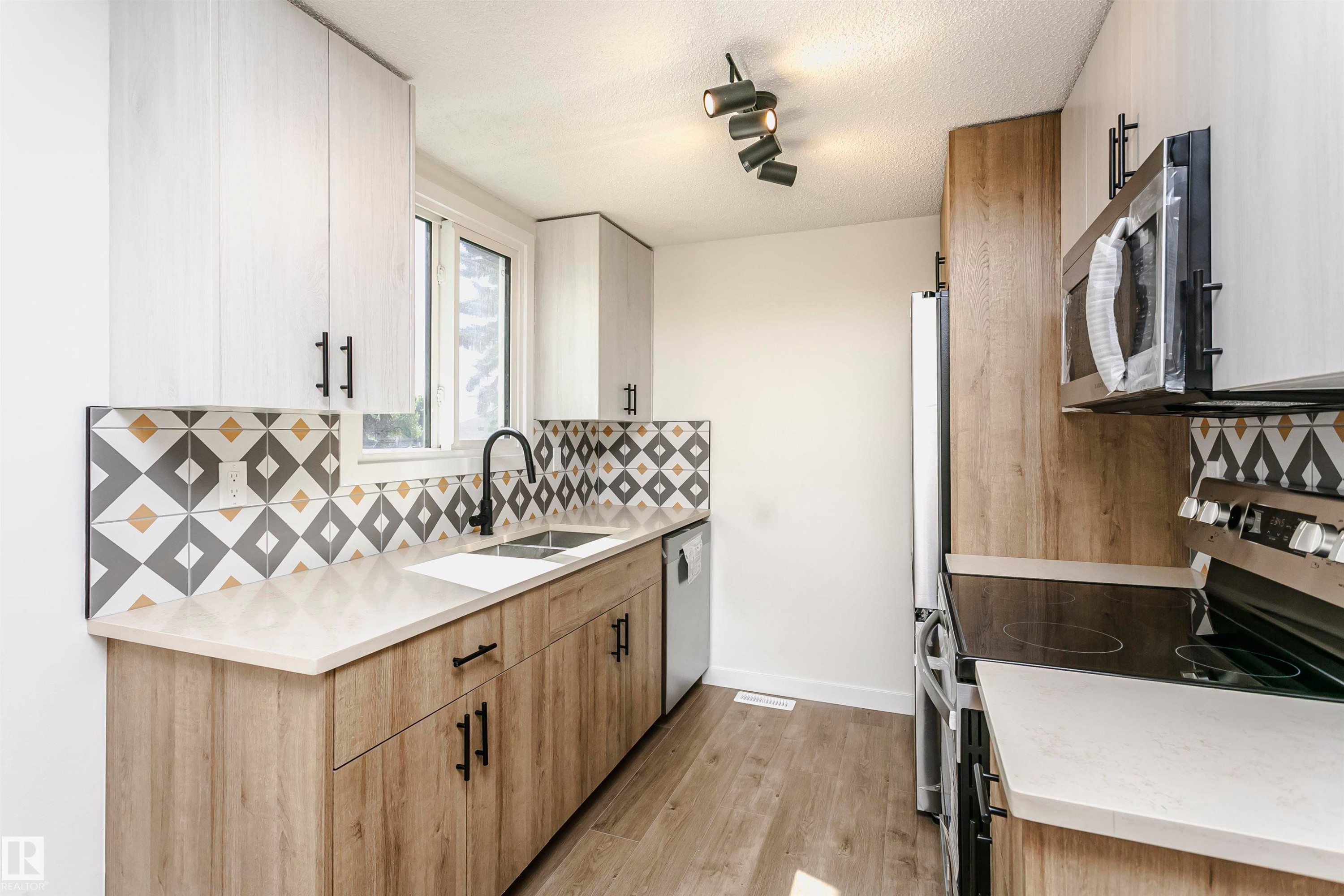 Contemporary kitchen featuring light wood-finish lower cabinetry and white upper cabinetry with black hardware - 5418 144B Avenue, Edmonton, AB