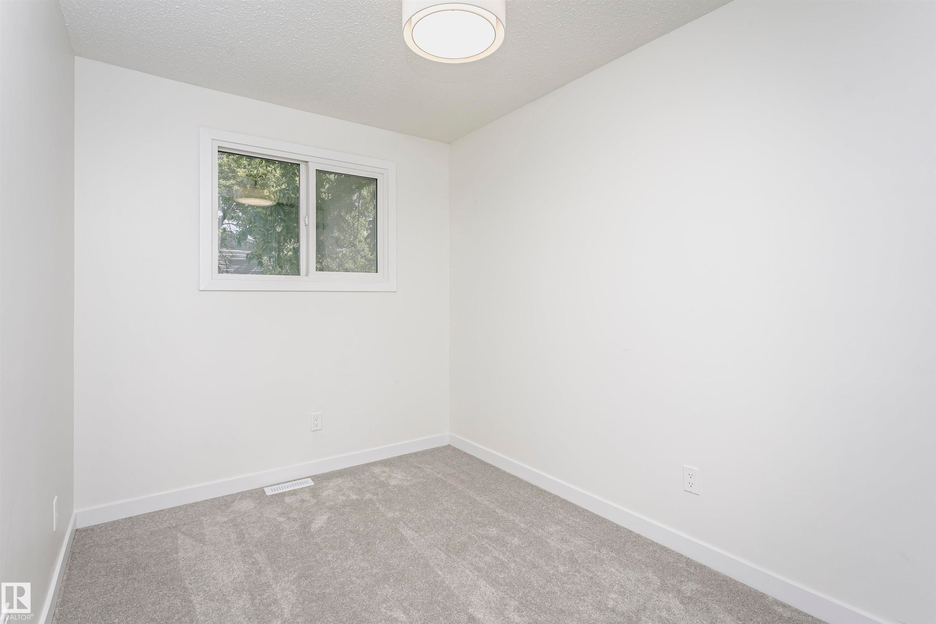 Room featuring light gray carpeting, white painted walls, white trim, a white window frame with operable sashes, and a flush-mount ceiling light fixture - 5418 144B Avenue, Edmonton, AB