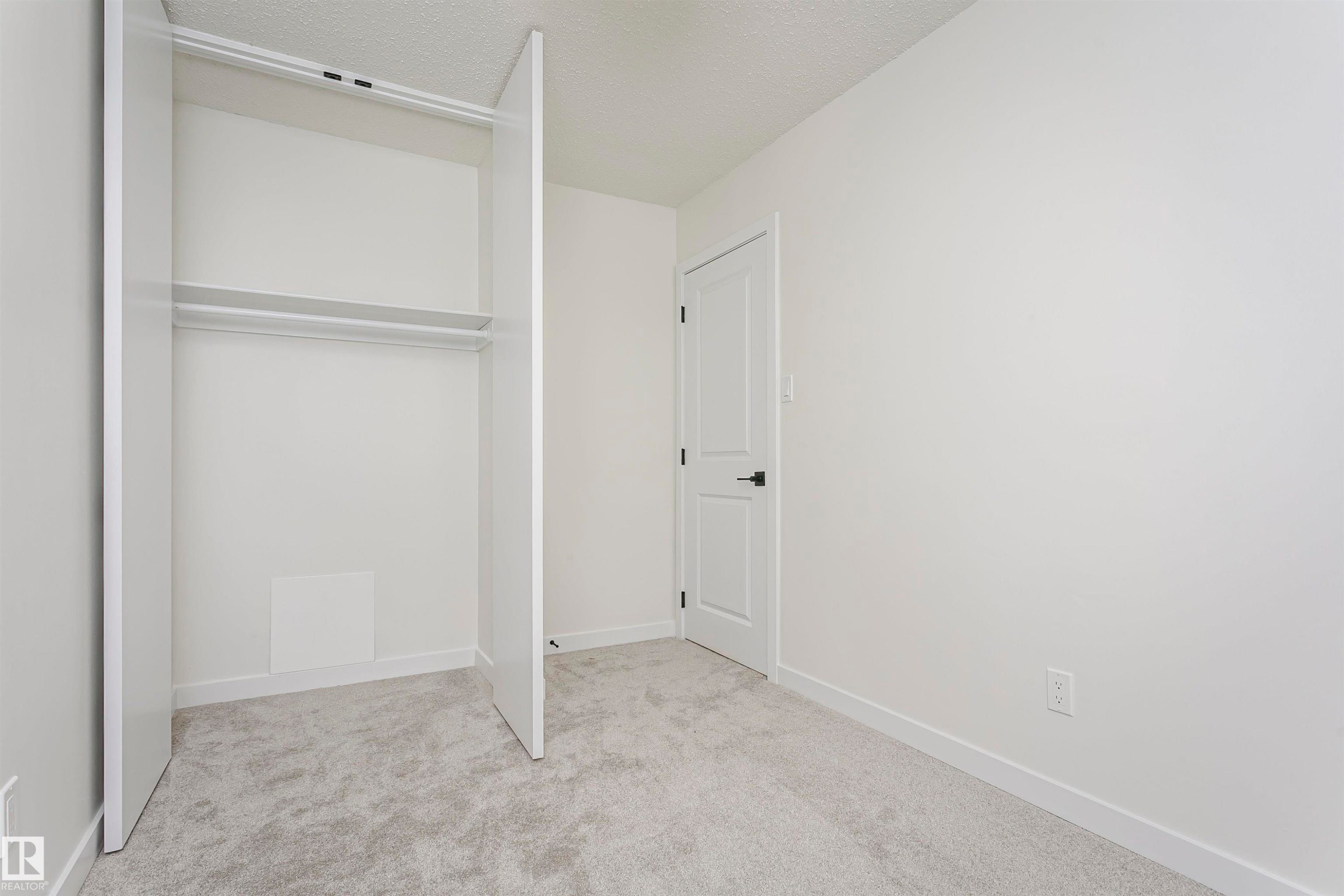 Bedroom featuring light gray carpeting, crisp white walls, a built-in closet with double hanging rods, and a white interior door with black hardware - 5418 144B Avenue, Edmonton, AB