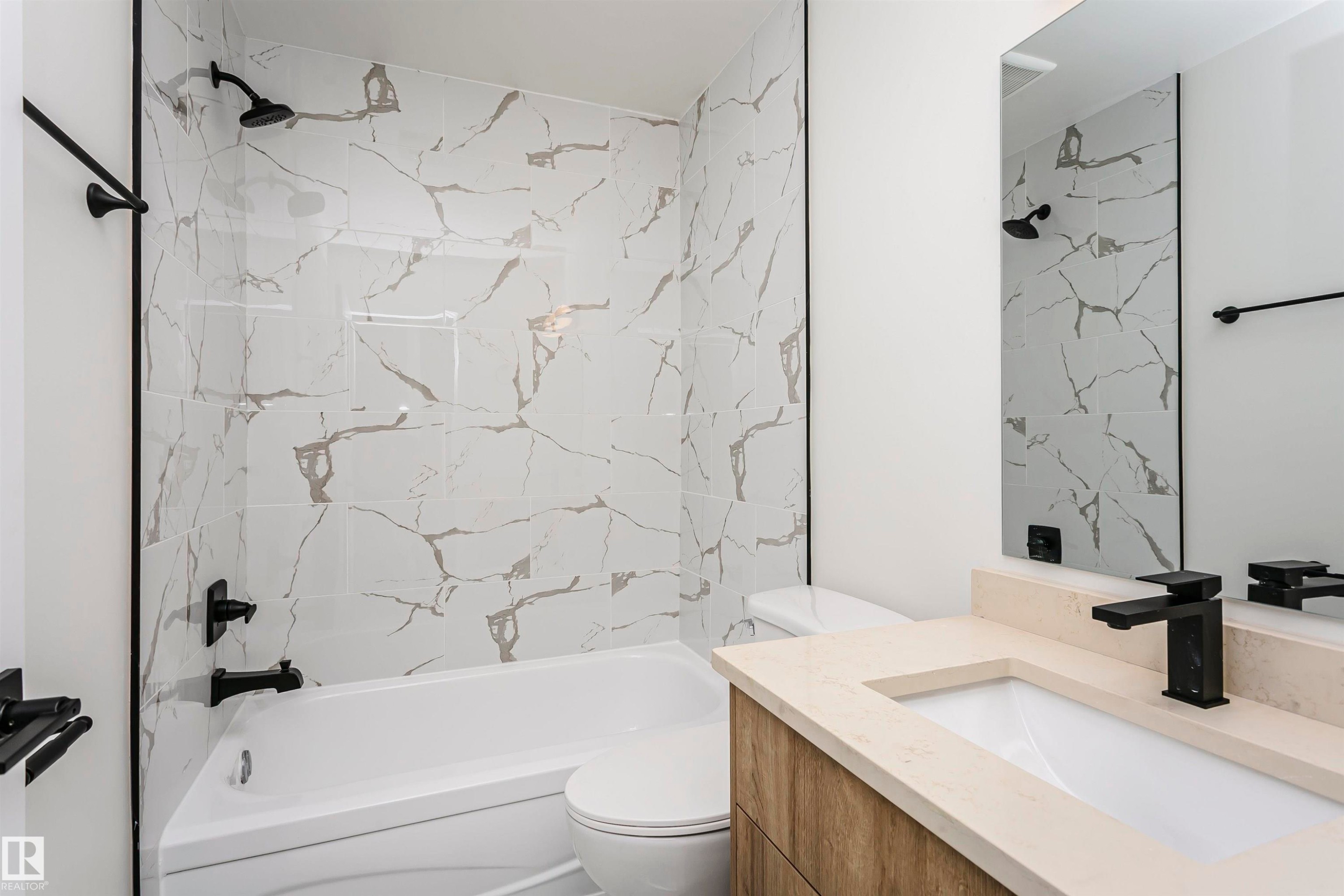 Bathroom featuring a shower-tub combination with white patterned tile surround, a white toilet, and a vanity with wood-finish cabinetry, light-toned countertop, and a rectangular undermount sink with a matte black faucet - 5418 144B Avenue, Edmonton, AB