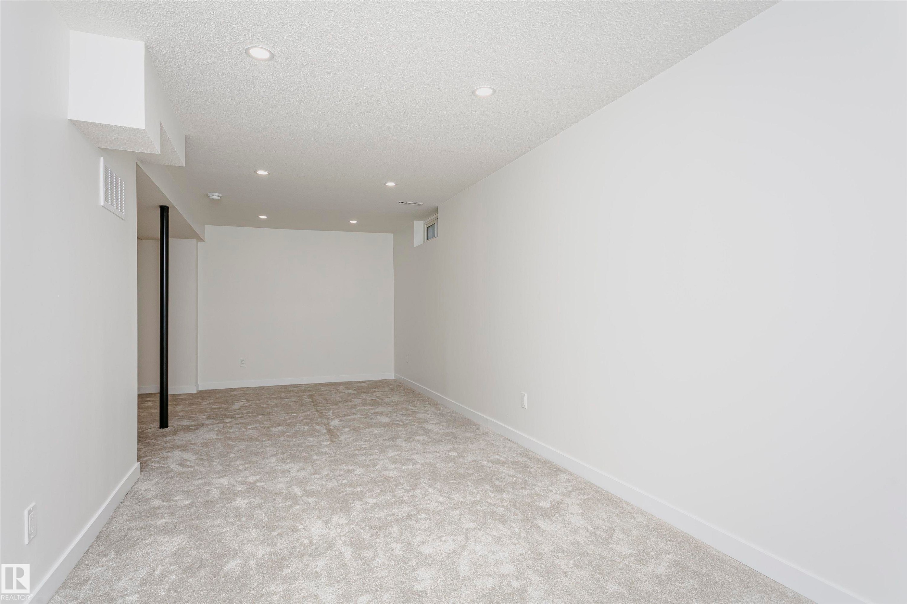 Spacious room featuring light gray carpet, white walls, recessed ceiling lighting, and white baseboards - 5418 144B Avenue, Edmonton, AB