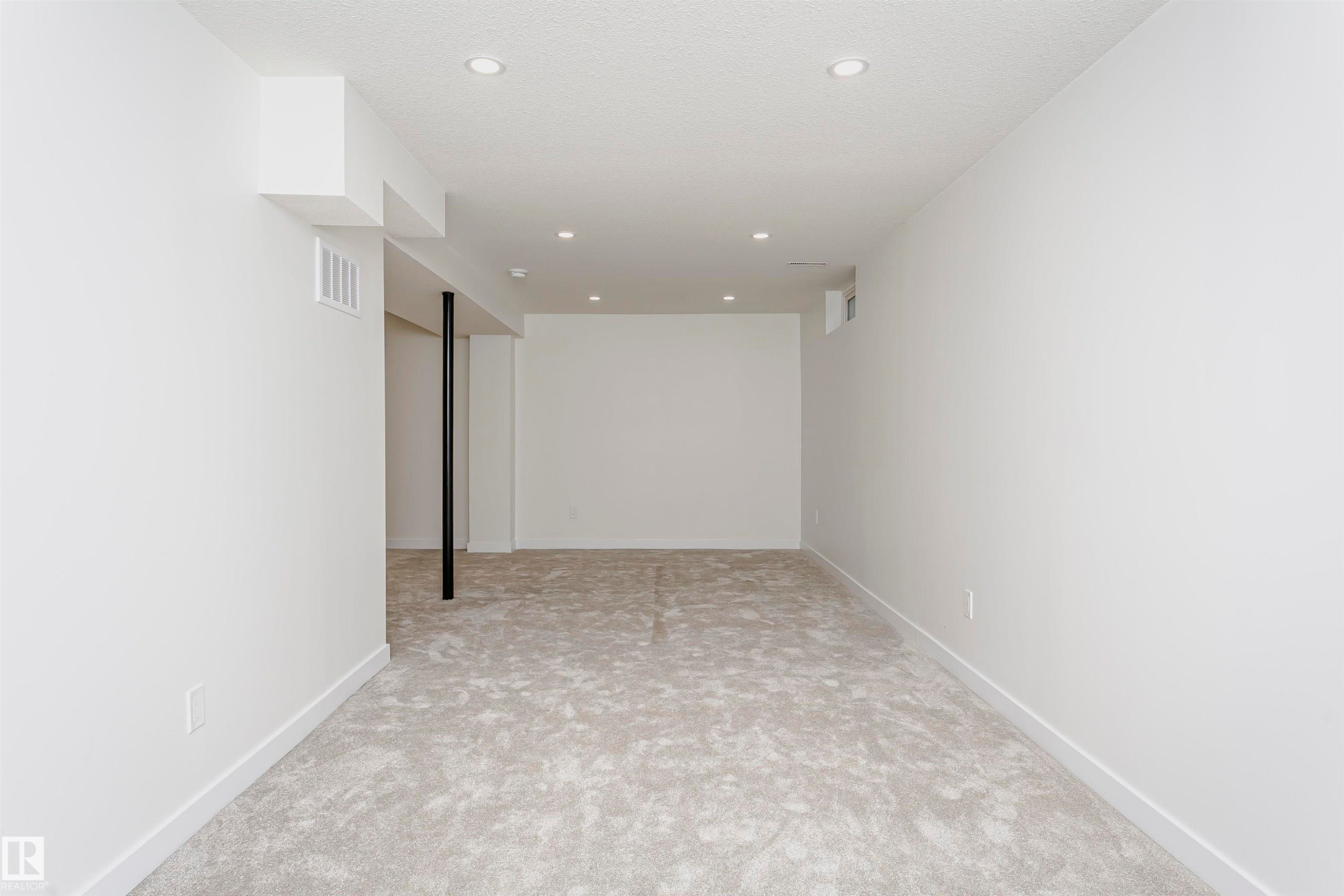 Spacious room featuring new light-toned carpeting, recessed ceiling lighting, crisp white walls, and contemporary white baseboards - 5418 144B Avenue, Edmonton, AB