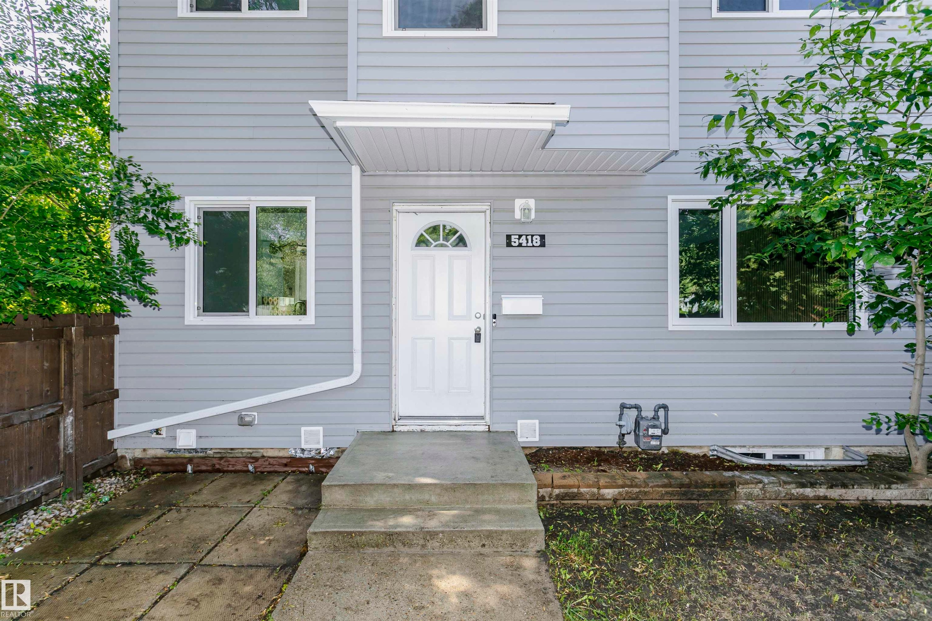 Light gray horizontal siding exterior with white trim windows and a white paneled entry door featuring an arched window detail - 5418 144B Avenue, Edmonton, AB