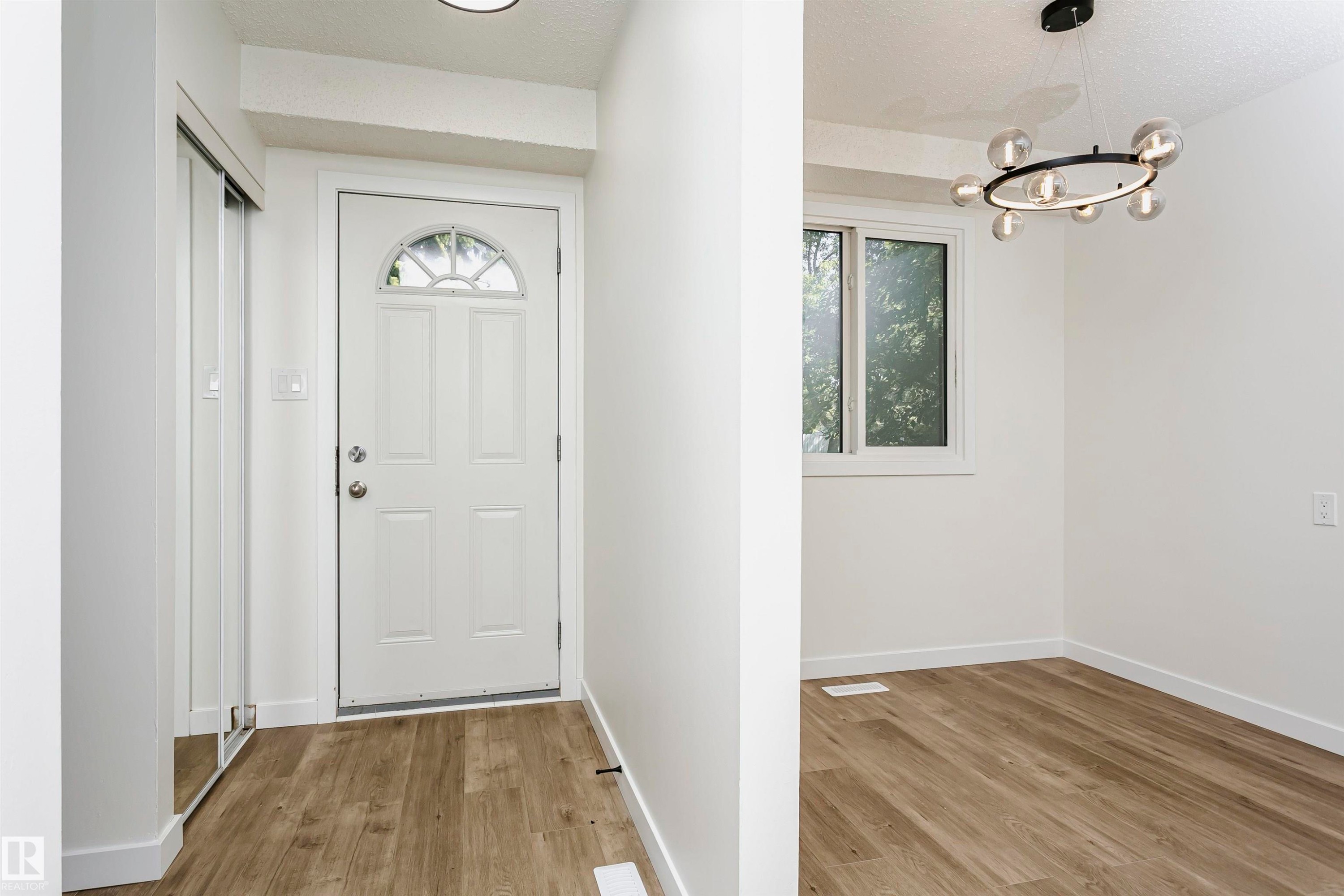 Bright entryway featuring a white paneled door with an arched transom window, wood-finish flooring, and a mirrored sliding closet door - 5418 144B Avenue, Edmonton, AB