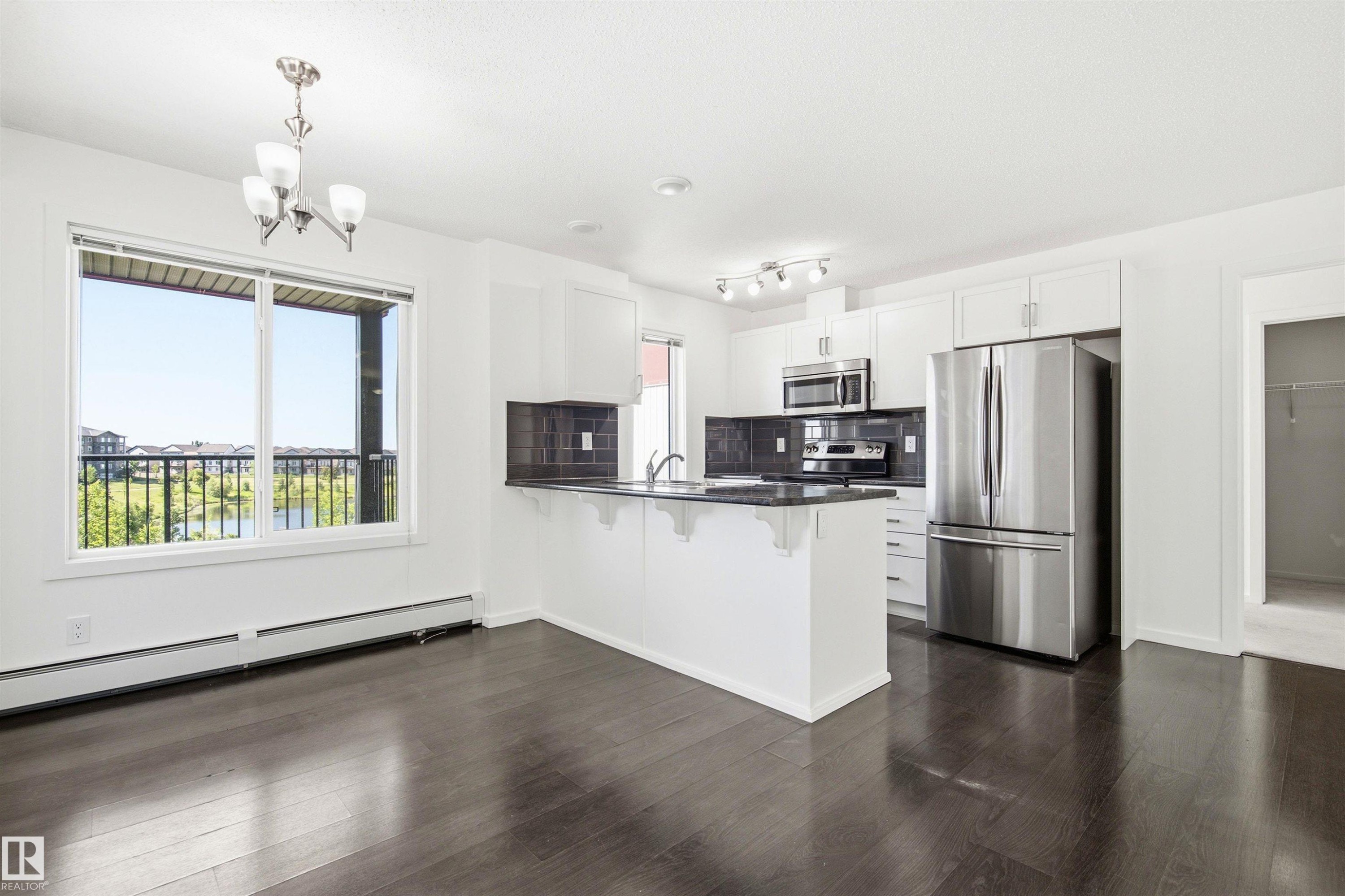 Open-concept kitchen and dining area featuring dark wood-finish flooring, white cabinetry, stainless steel appliances, and a central island with a sink - 435 5515 7 Avenue, Edmonton, AB