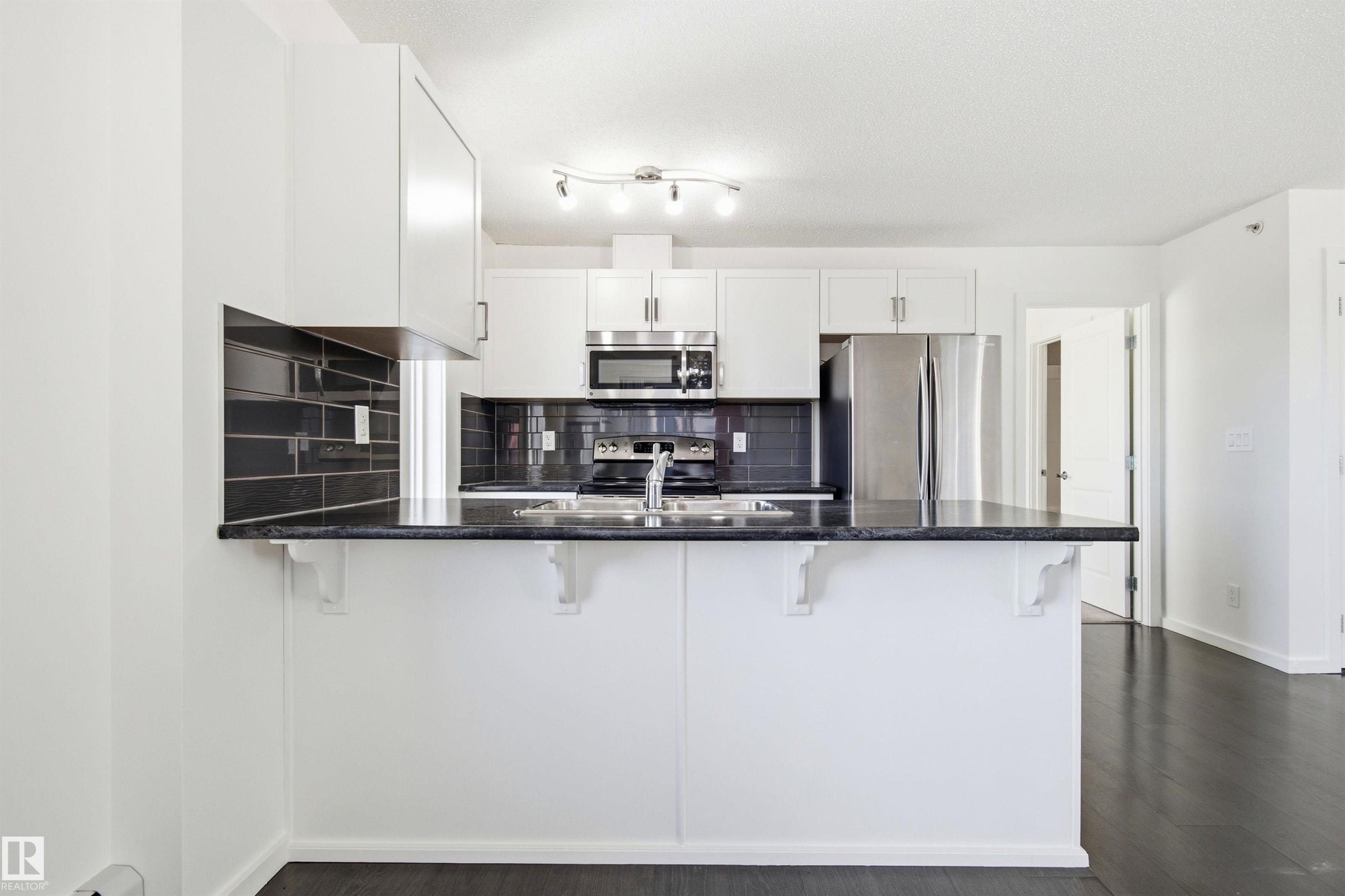 Modern kitchen featuring white cabinetry, dark stone countertops, and a black subway tile backsplash - 435 5515 7 Avenue, Edmonton, AB