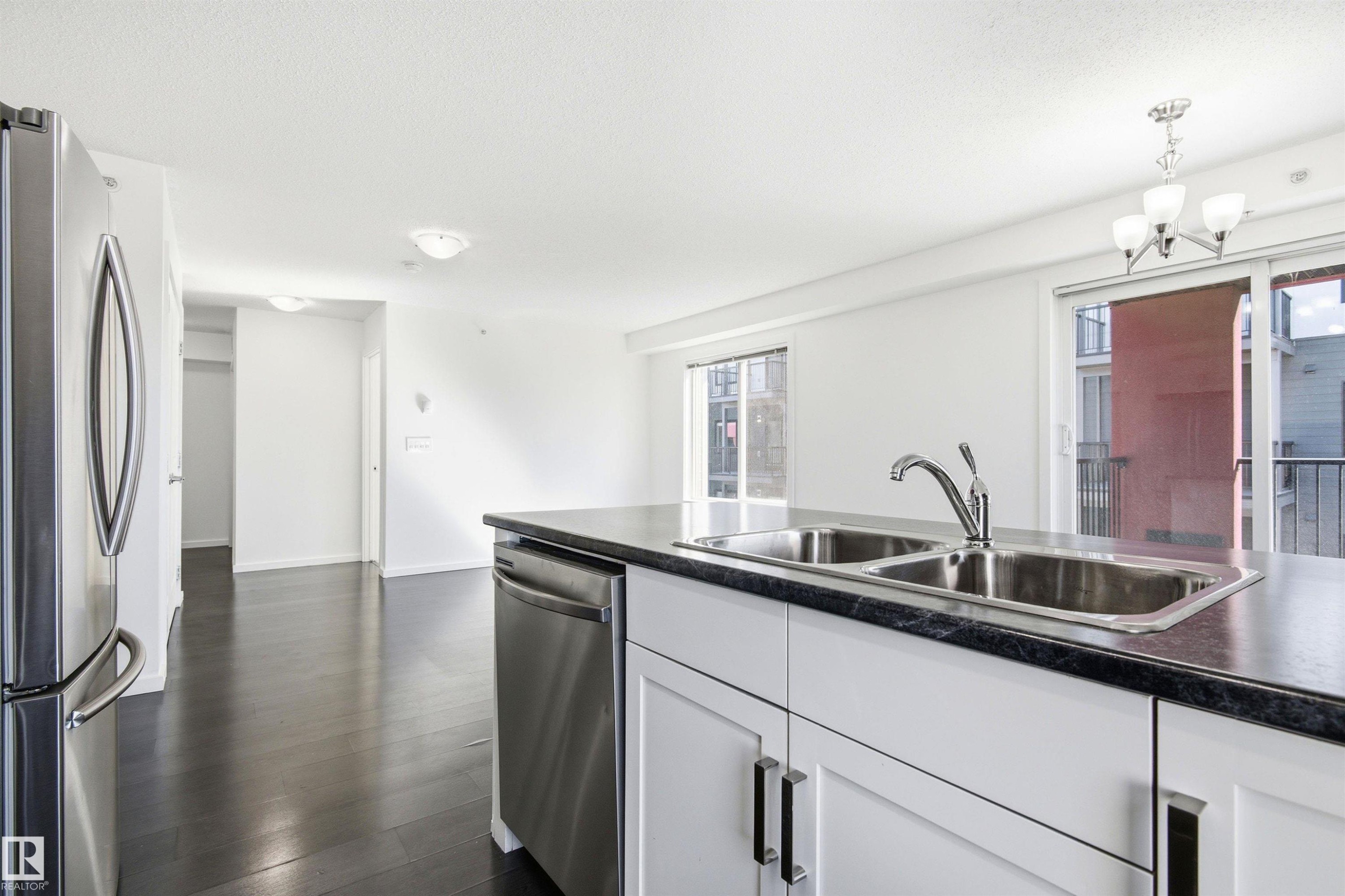 Kitchen island featuring a double-basin stainless steel sink with a single-handle faucet, integrated stainless steel dishwasher, and dark countertop - 435 5515 7 Avenue, Edmonton, AB