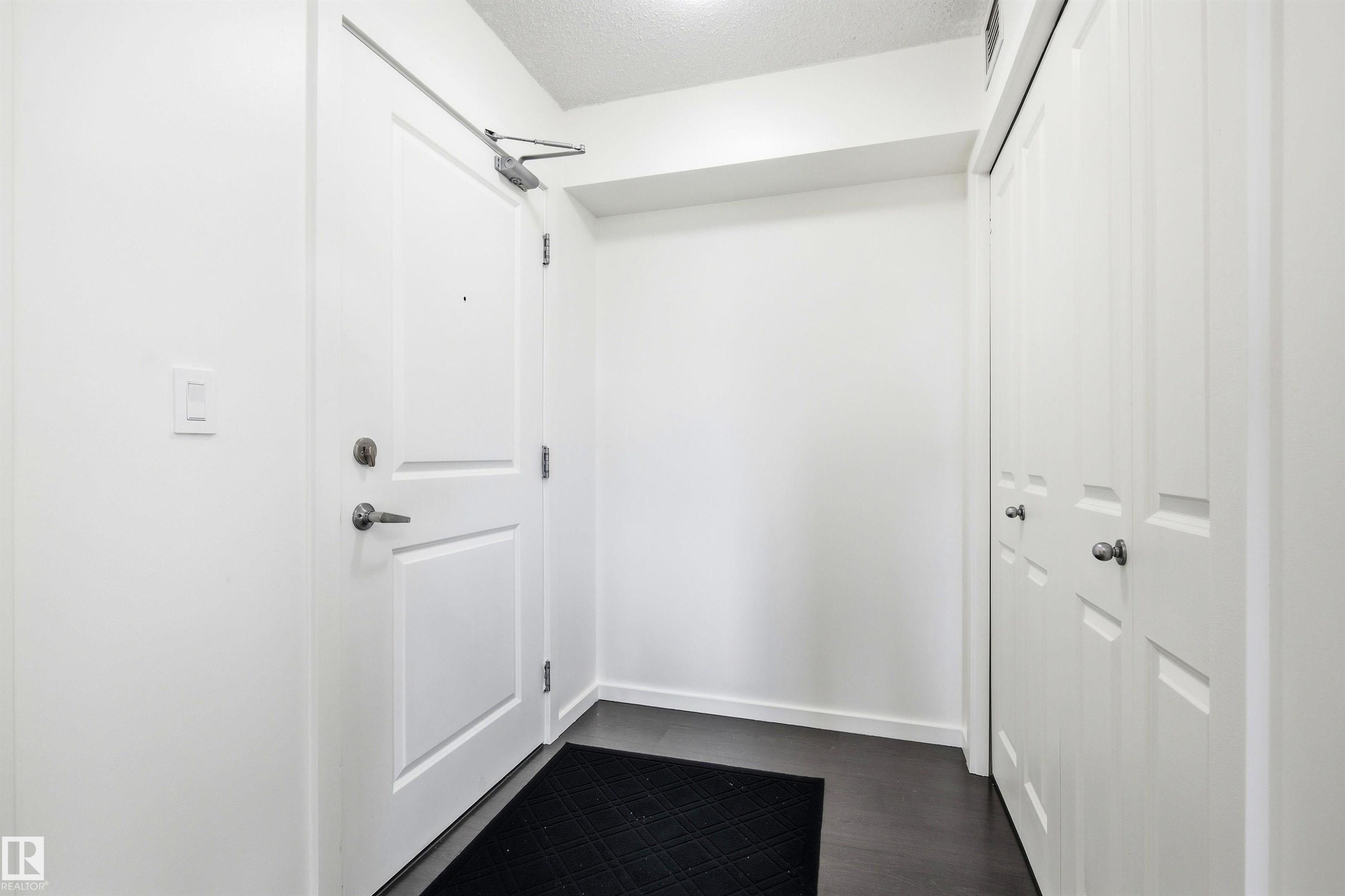 Entryway featuring dark wood-finish flooring, white walls, and a white paneled door with brushed nickel hardware - 435 5515 7 Avenue, Edmonton, AB
