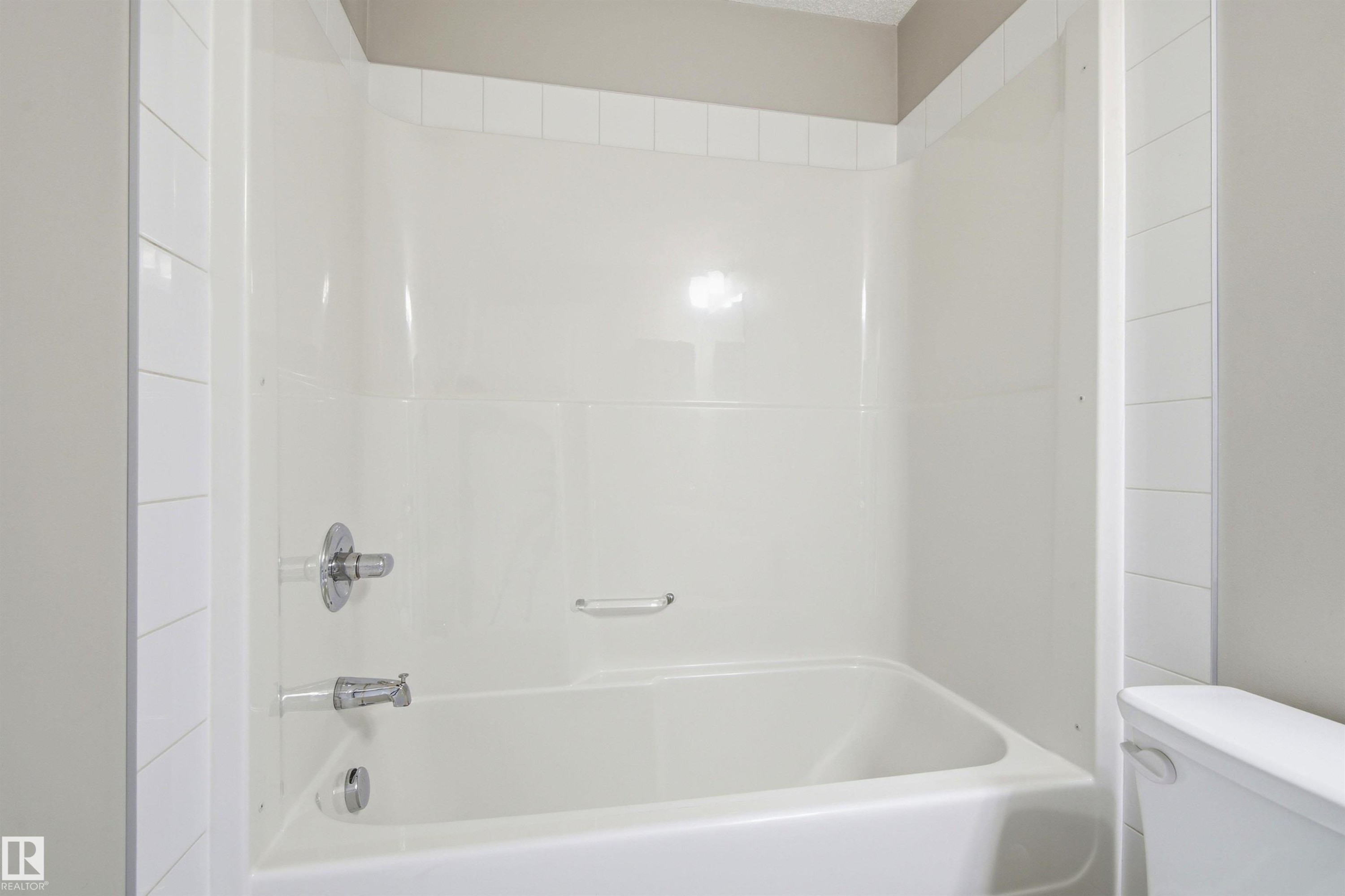 White bathtub with integrated shower surround, chrome fixtures, and coordinating white tile trim - 435 5515 7 Avenue, Edmonton, AB