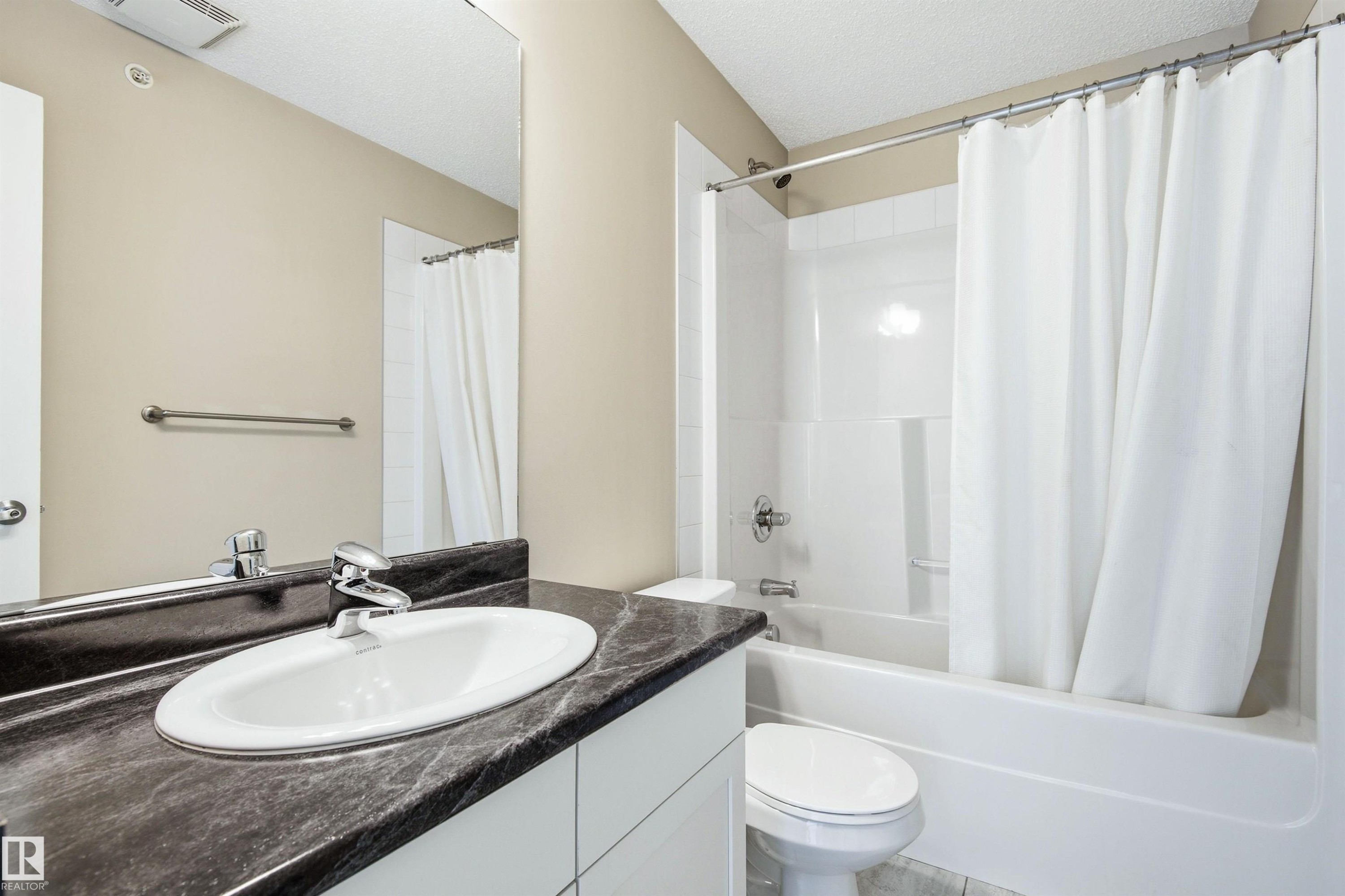 Bathroom featuring a dark-toned countertop with an integrated white sink, chrome faucet, and a large wall-mounted mirror - 435 5515 7 Avenue, Edmonton, AB
