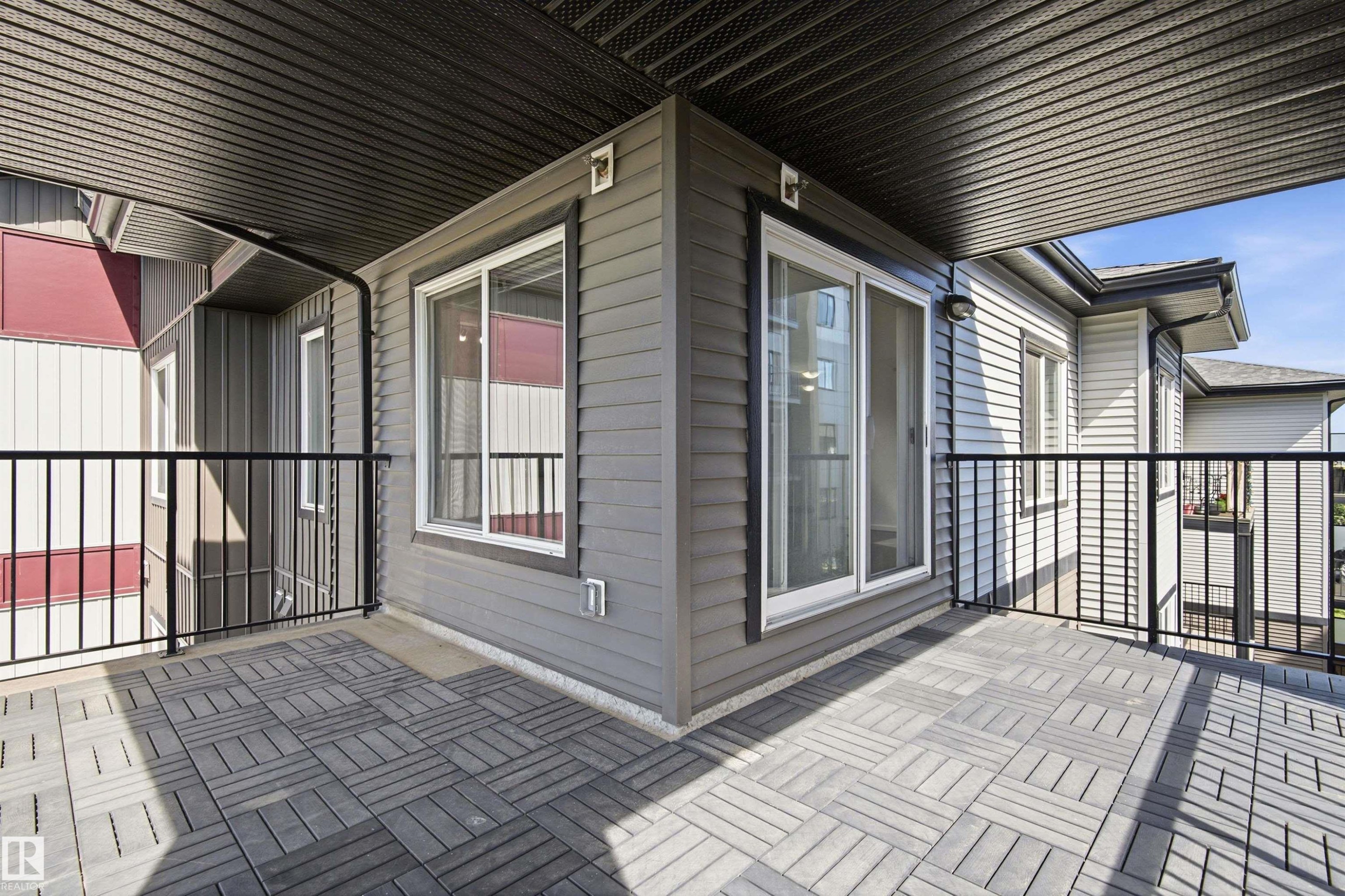 Spacious outdoor balcony featuring patterned paving, dark metal railings, and a dark soffit ceiling - 435 5515 7 Avenue, Edmonton, AB