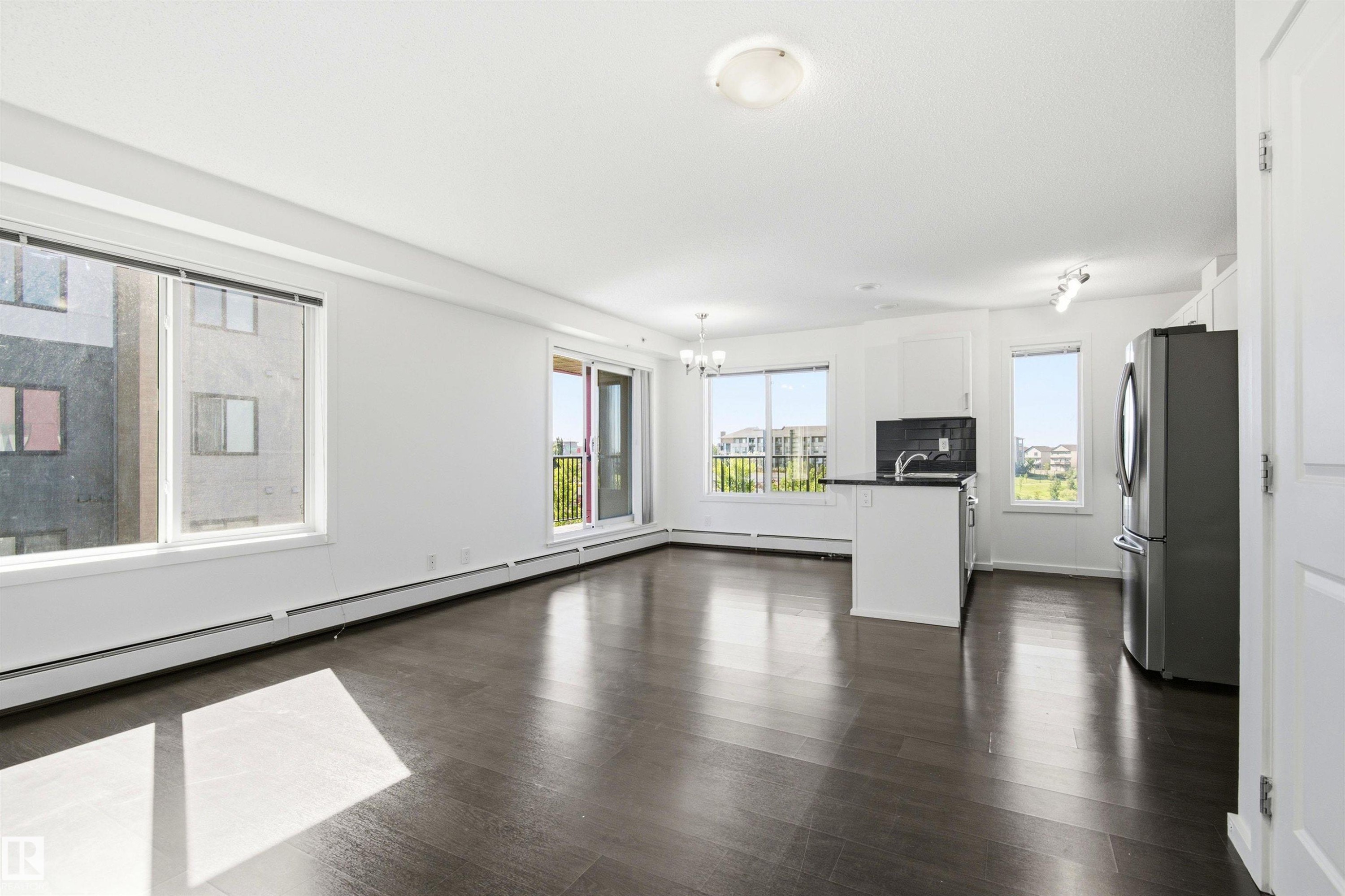 Open-concept living space featuring dark wood-finish flooring, white walls, and multiple windows for natural illumination - 435 5515 7 Avenue, Edmonton, AB
