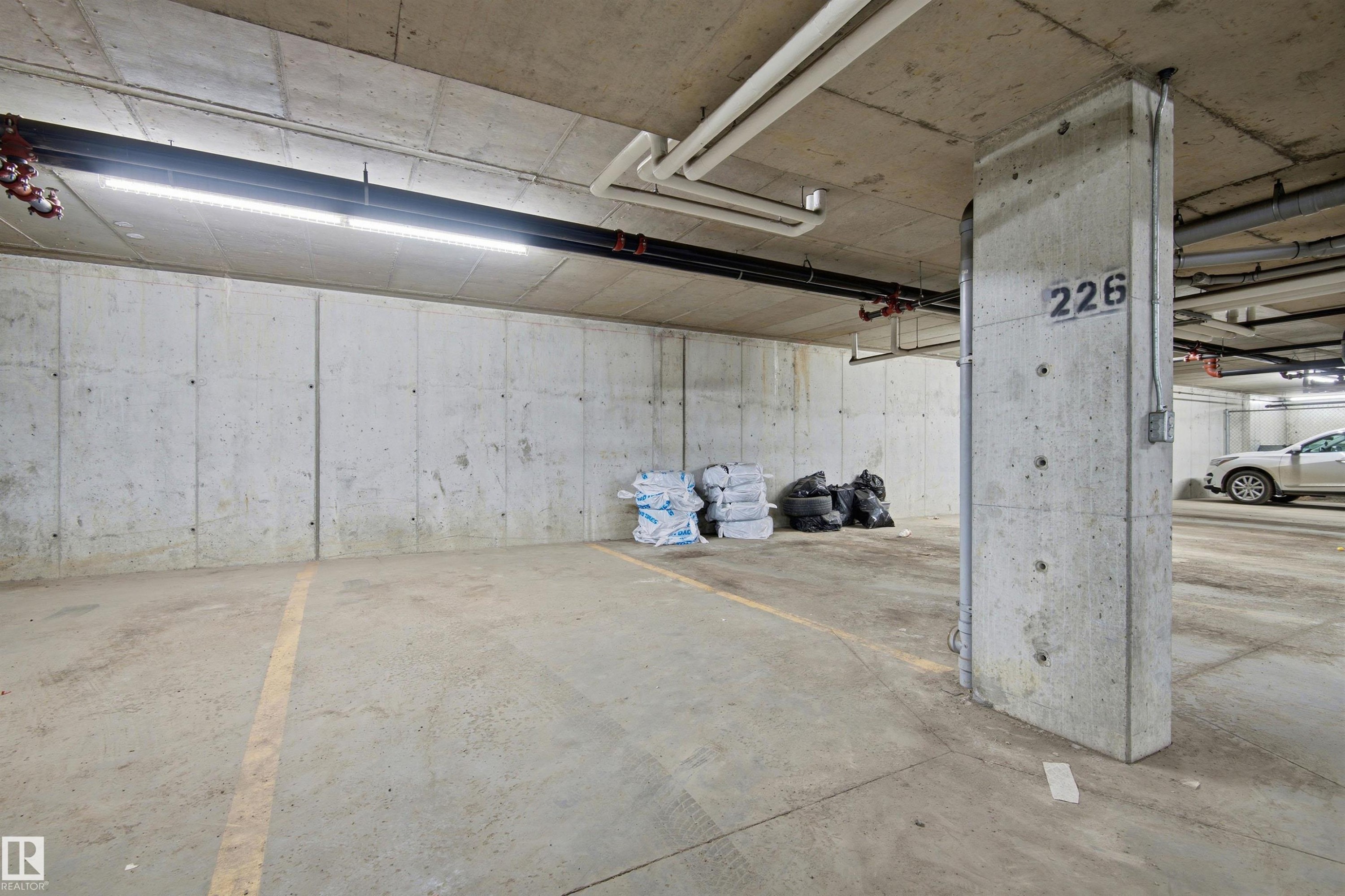 Dedicated parking stall 226 featuring concrete walls and ceiling, overhead lighting, and visible utility conduits - 435 5515 7 Avenue, Edmonton, AB