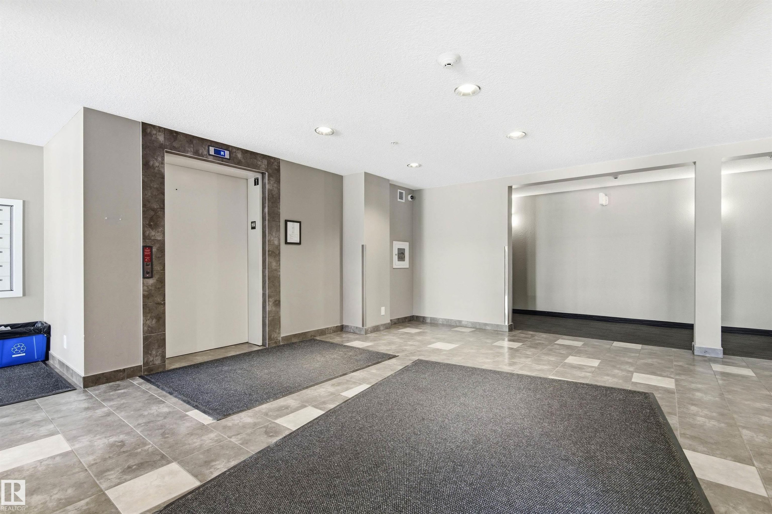 Entrance lobby featuring a centered elevator with stone-look surround, recessed lighting, and tile flooring - 435 5515 7 Avenue, Edmonton, AB