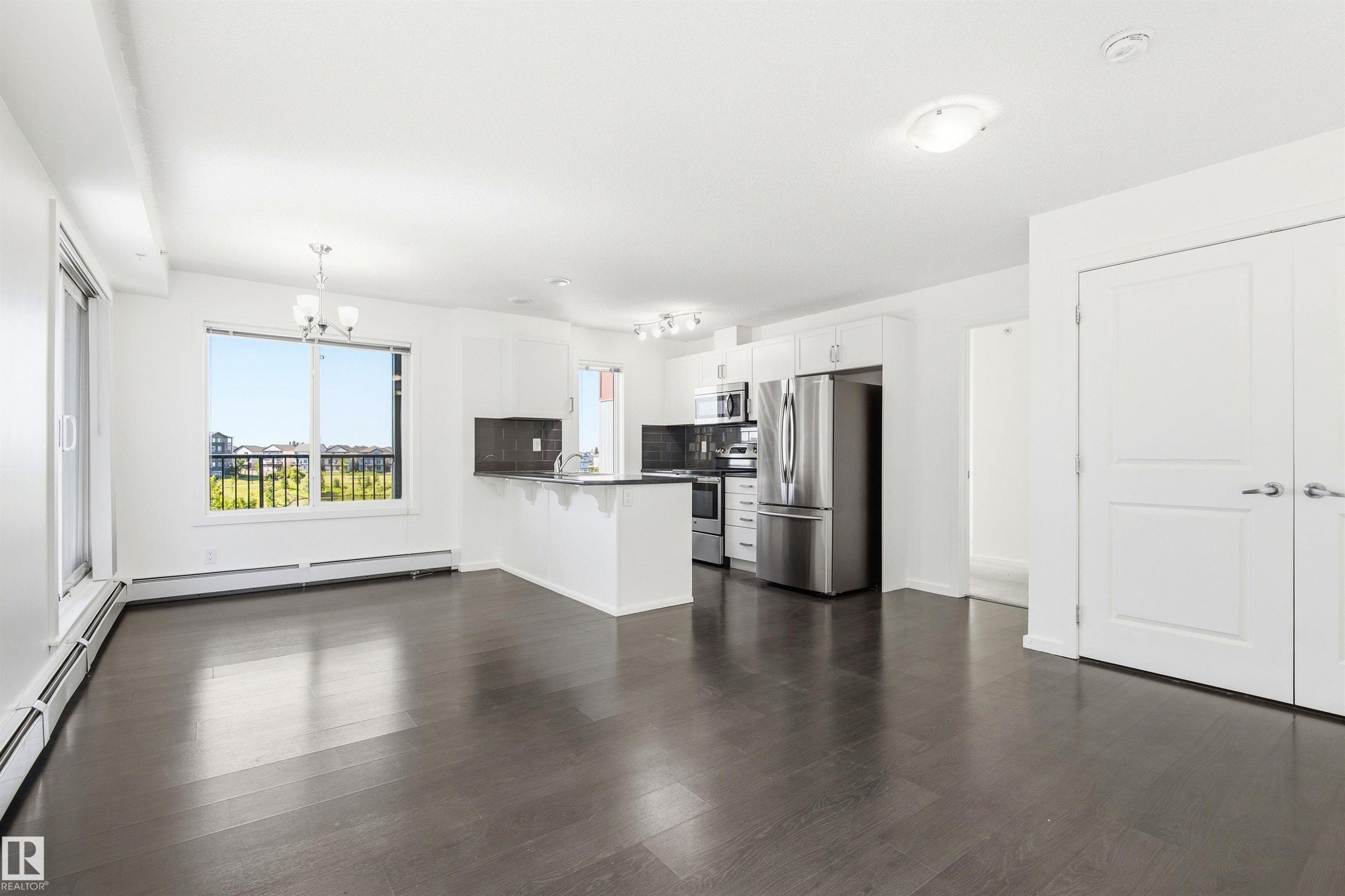 Open-concept living space featuring wood-finish flooring and a bright kitchen with stainless steel appliances - 435 5515 7 Avenue, Edmonton, AB