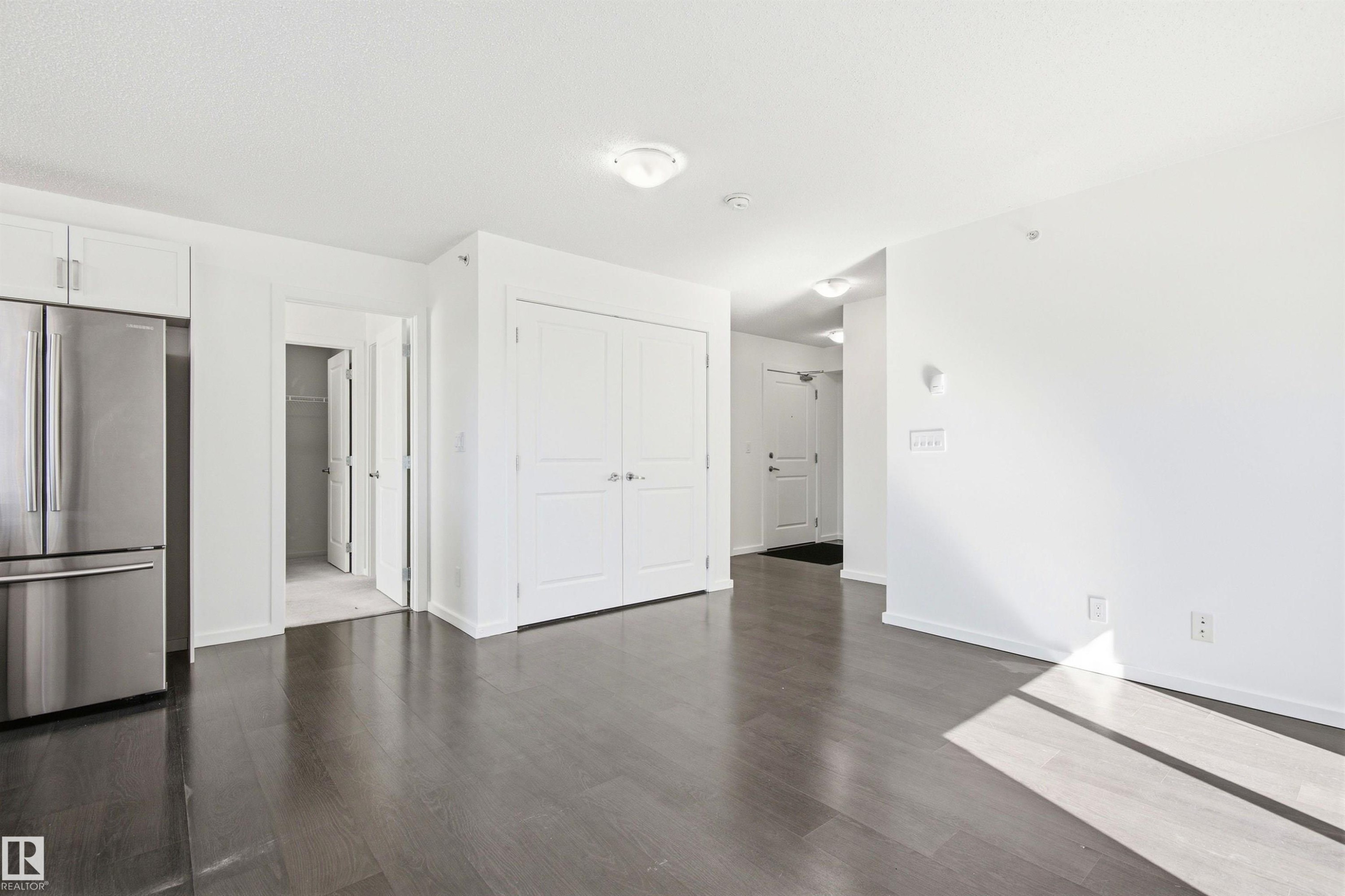 Expansive open-concept living area featuring dark wood-finish flooring and bright white walls - 435 5515 7 Avenue, Edmonton, AB