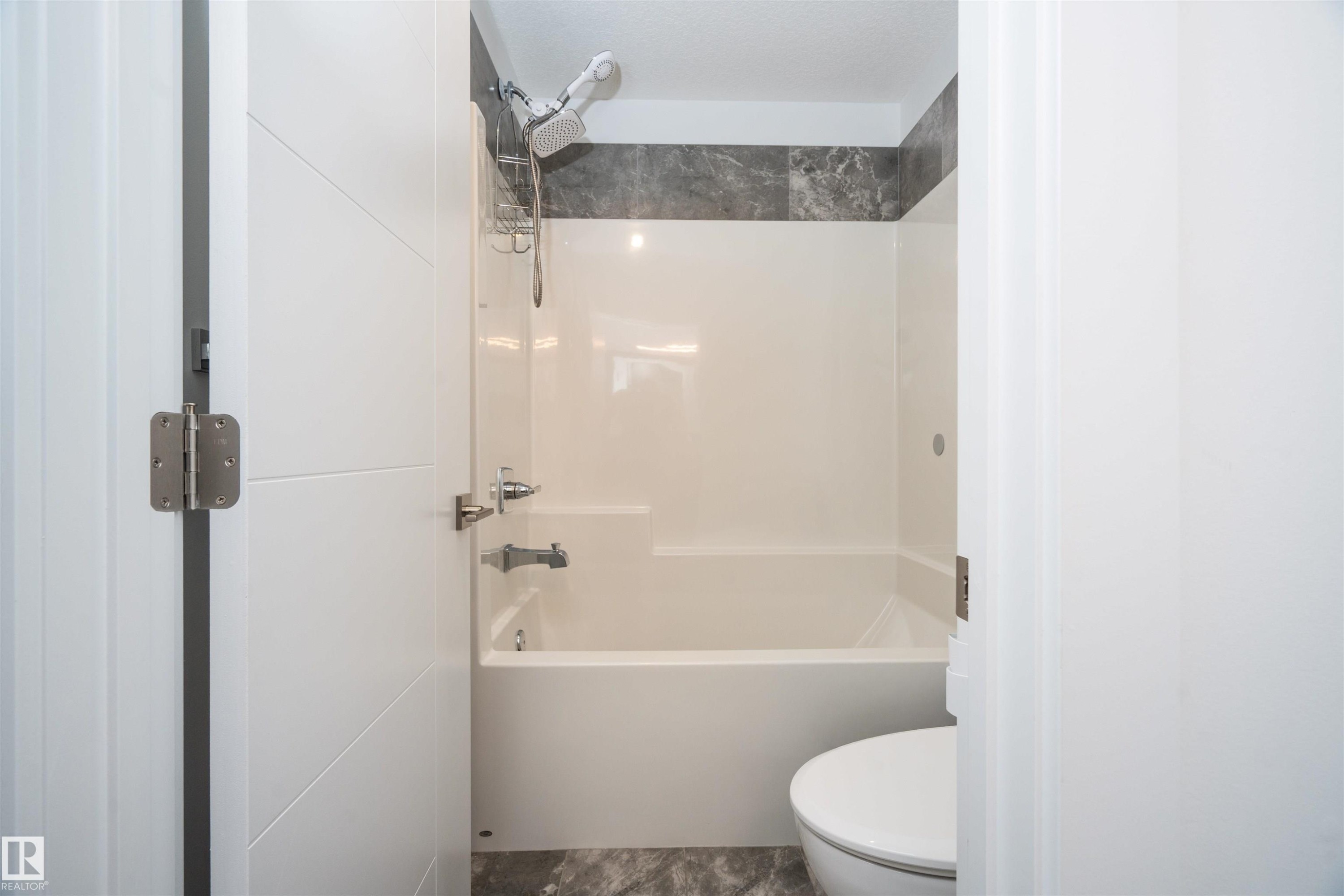 Full bathroom featuring a white tub-shower combination with a dark gray tiled surround and a coordinating gray stone-finish floor - 4714 Charles Bay Bay, Edmonton, AB