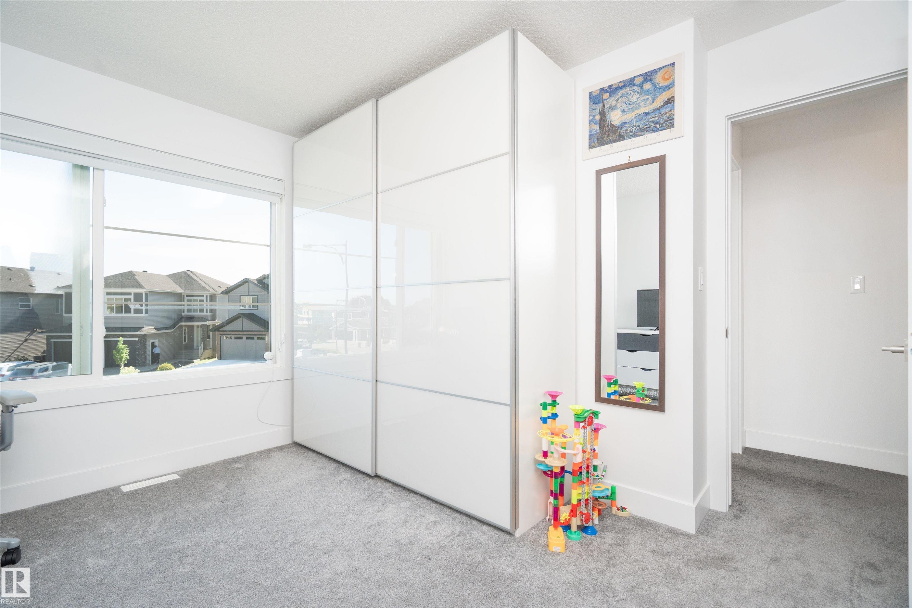 Bright room featuring a large window, light gray carpet, and white built-in cabinetry with sliding doors - 4714 Charles Bay Bay, Edmonton, AB