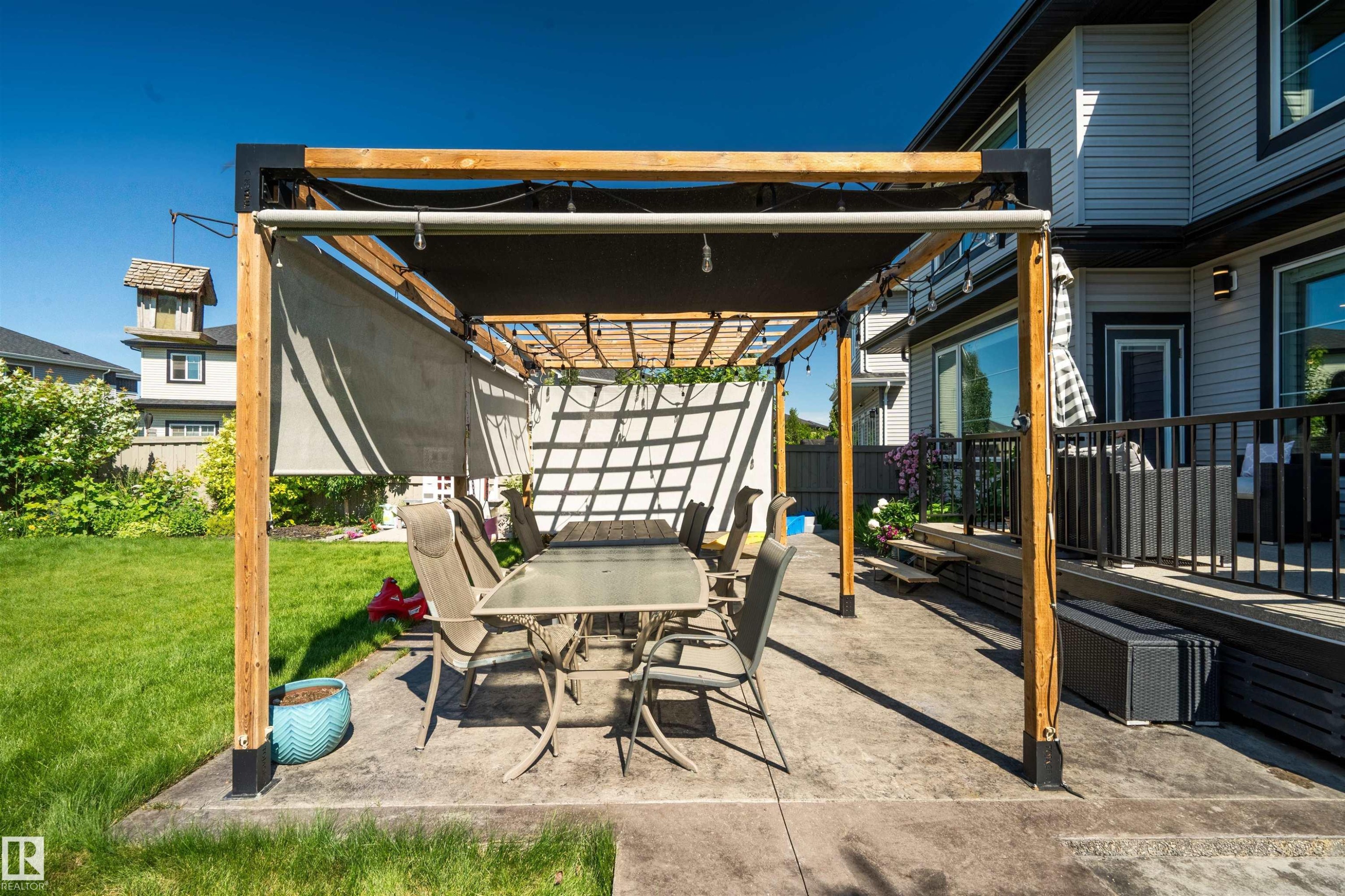 Outdoor patio featuring a pergola with a retractable shade cover, an expansive lawn, and a multi-level deck with black railings - 4714 Charles Bay Bay, Edmonton, AB