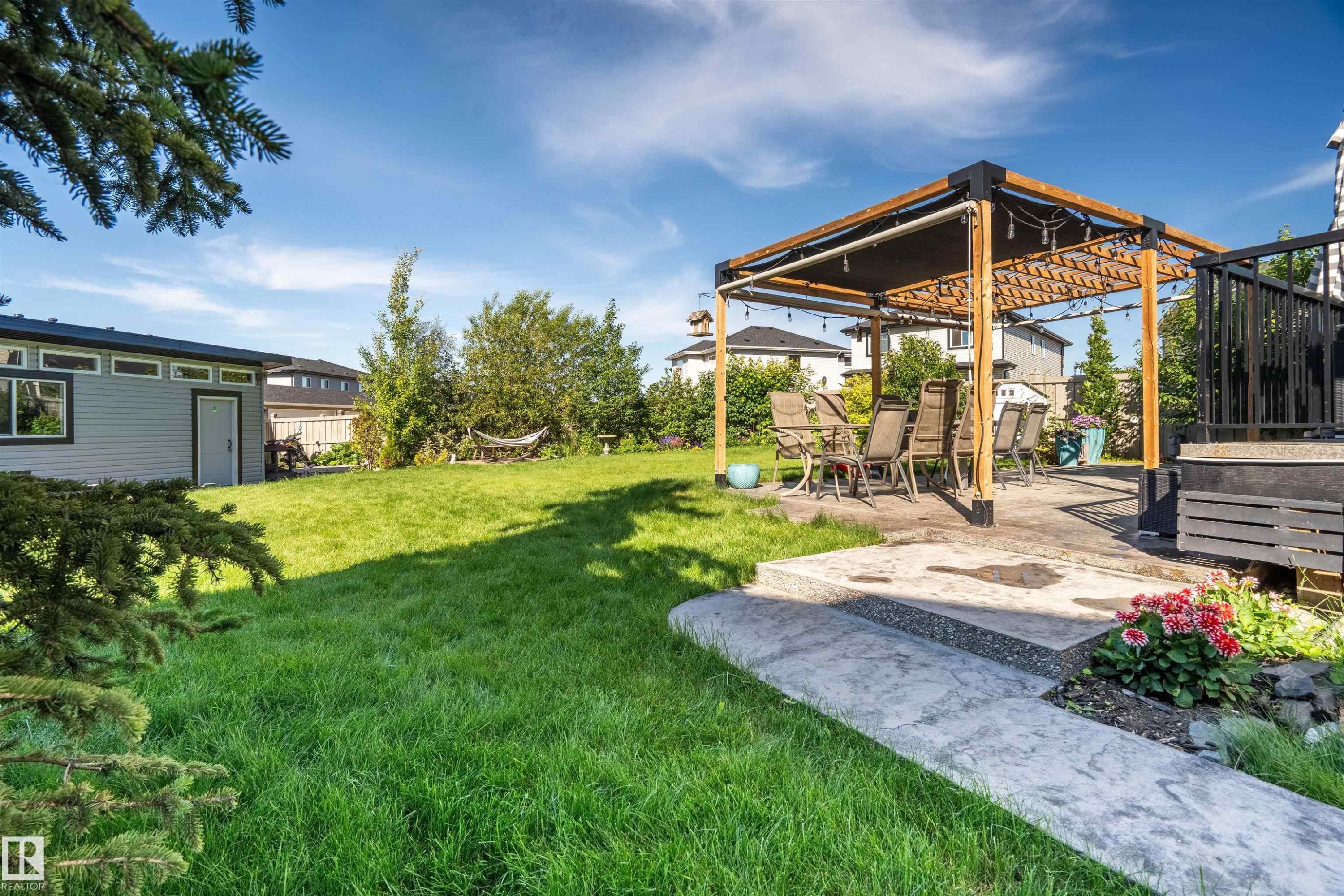 Expansive backyard featuring a large green space, a modern pergola on a concrete patio, a detached shed with horizontal siding, a black composite deck, and mature trees - 4714 Charles Bay Bay, Edmonton, AB