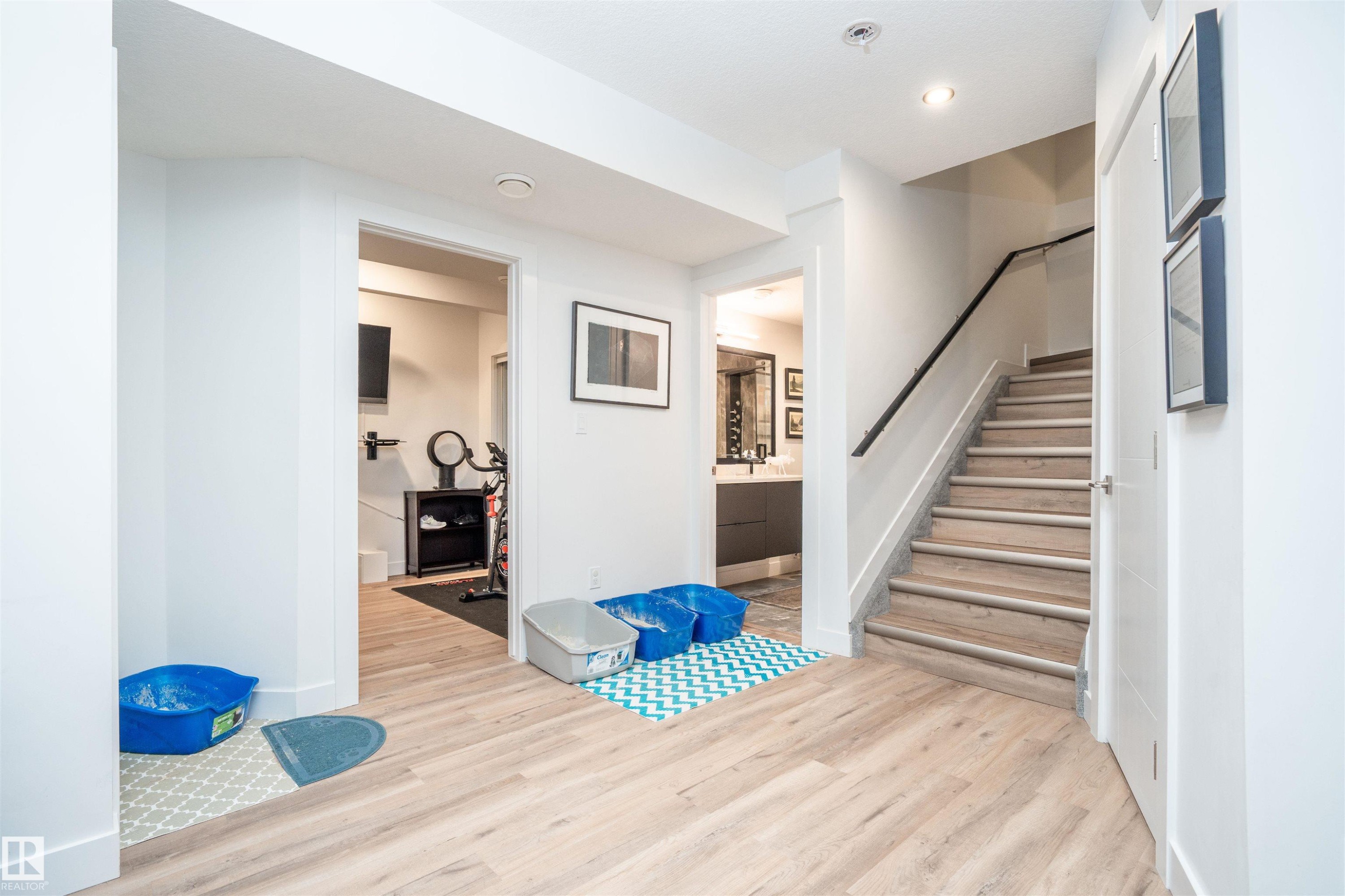 Light wood-finish flooring extending through a lower-level hallway with a staircase featuring a dark handrail and white risers - 4714 Charles Bay Bay, Edmonton, AB