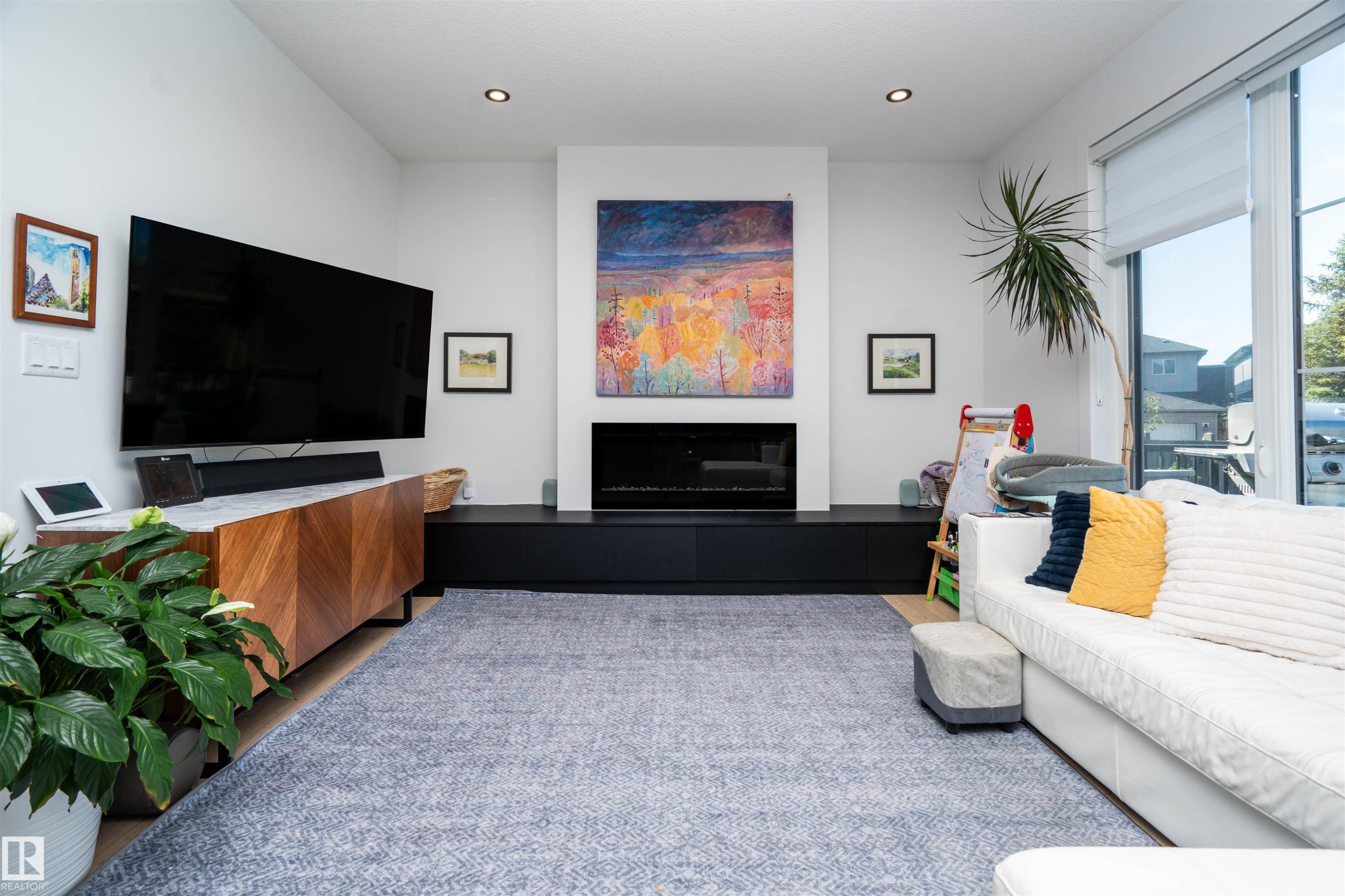 Living room featuring a prominent fireplace with a dark-finished hearth, recessed lighting, and light wood-finish flooring - 4714 Charles Bay Bay, Edmonton, AB