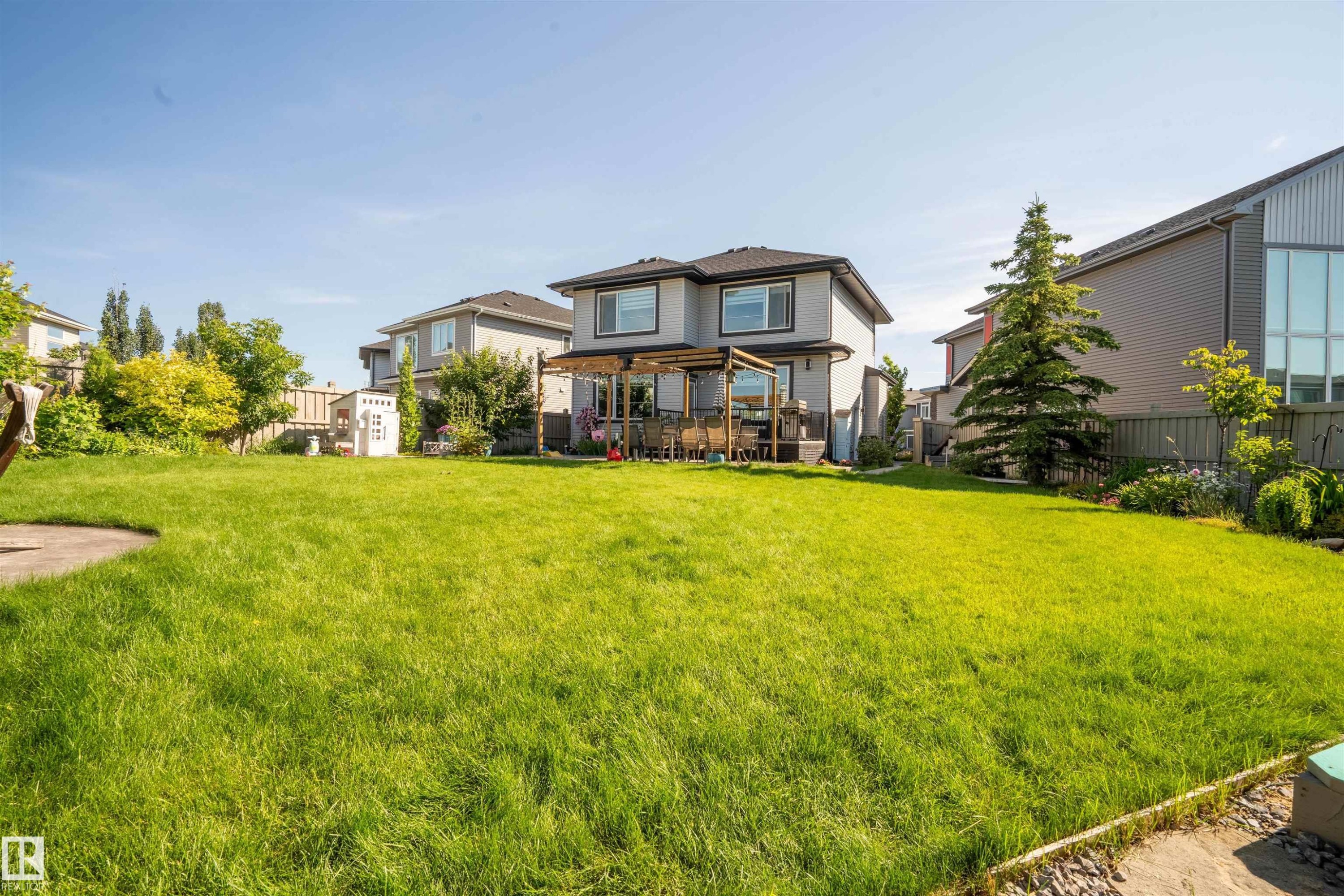 Spacious rear yard featuring an expansive lawn, a two-story residence with a back deck, and mature landscaping elements - 4714 Charles Bay Bay, Edmonton, AB