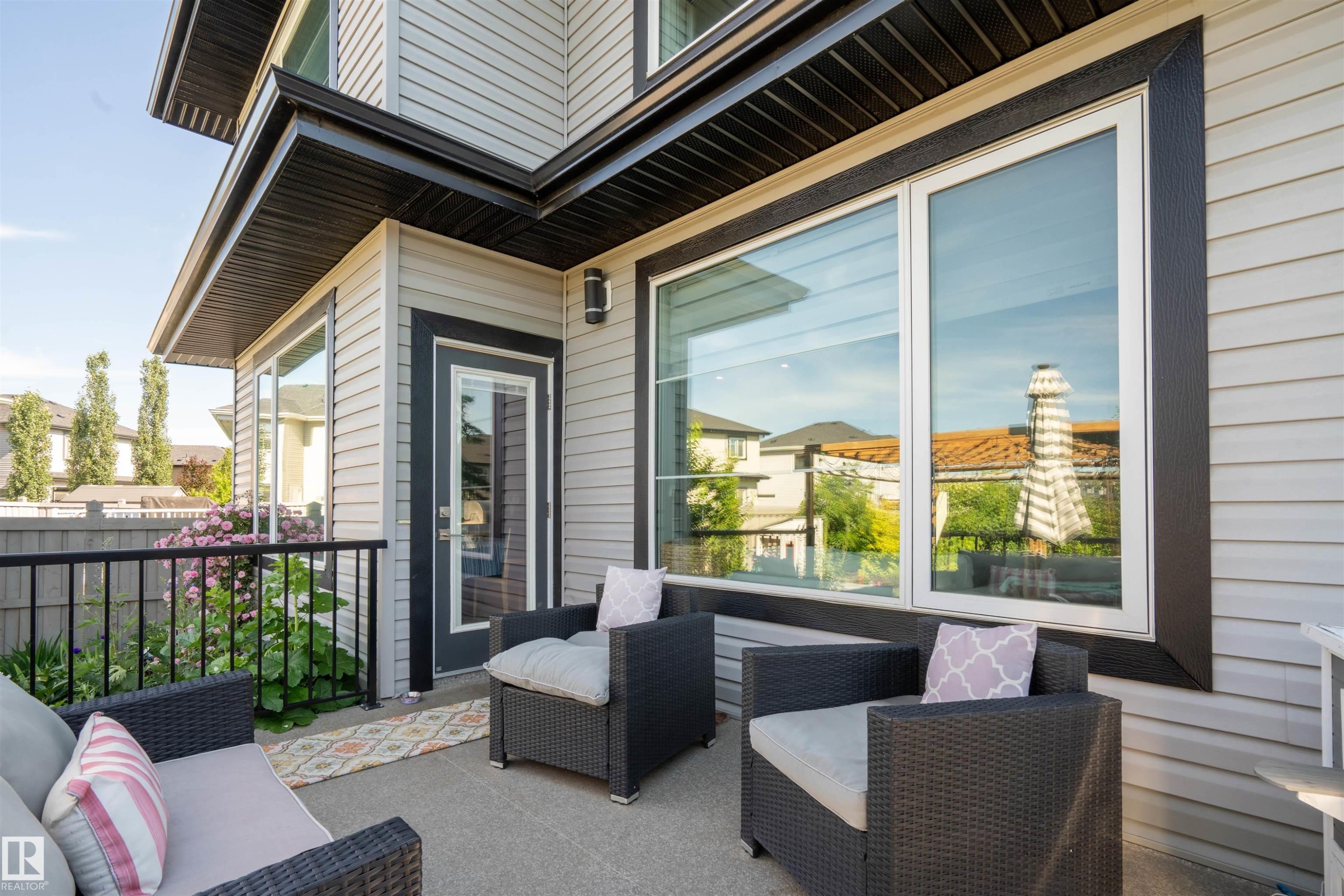Outdoor concrete patio featuring a glass-paneled door, large windows, and a black metal railing - 4714 Charles Bay Bay, Edmonton, AB