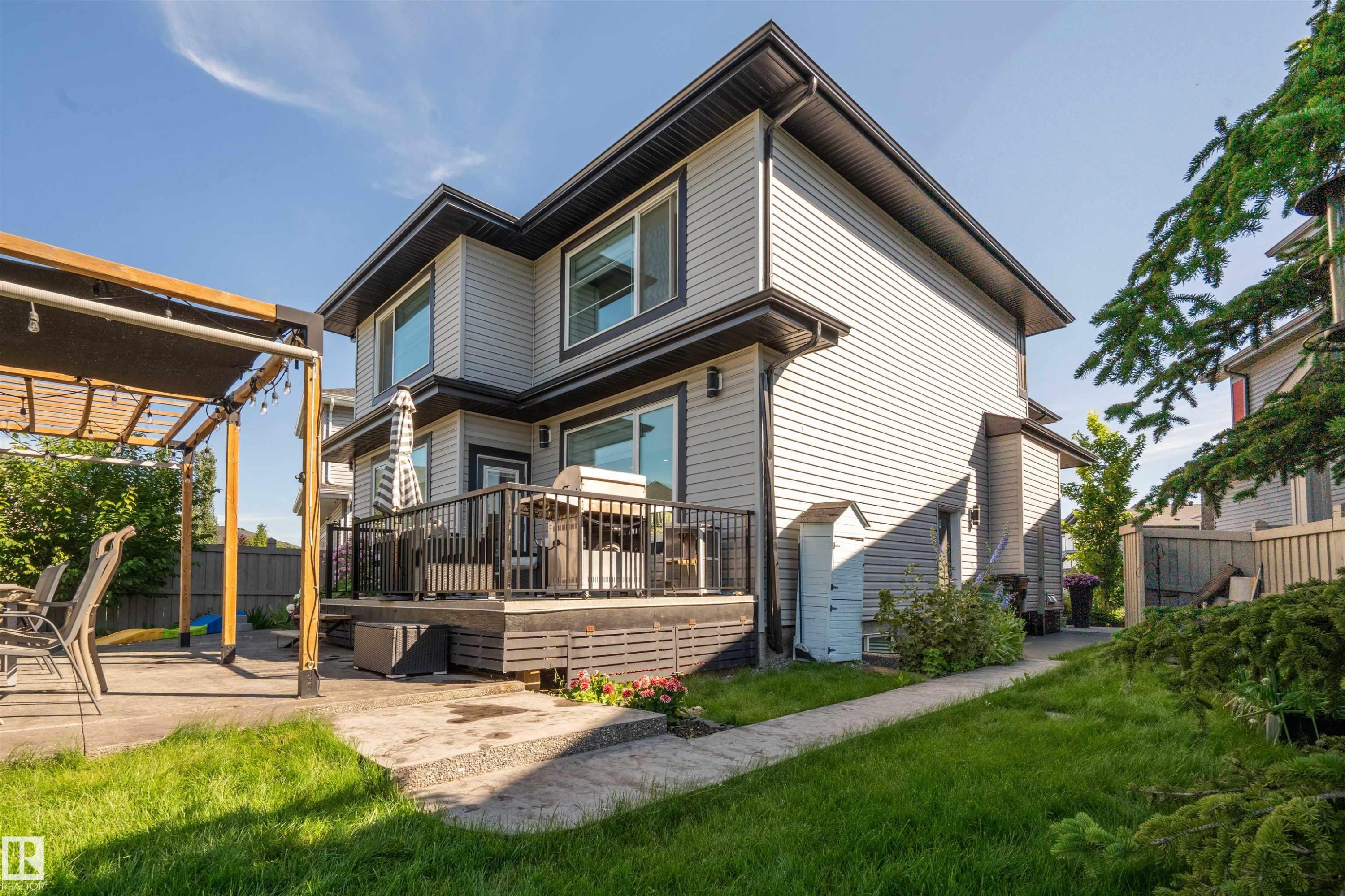 Rear exterior featuring a multi-level deck with black railing, a concrete patio, and a wood pergola with a retractable shade - 4714 Charles Bay Bay, Edmonton, AB