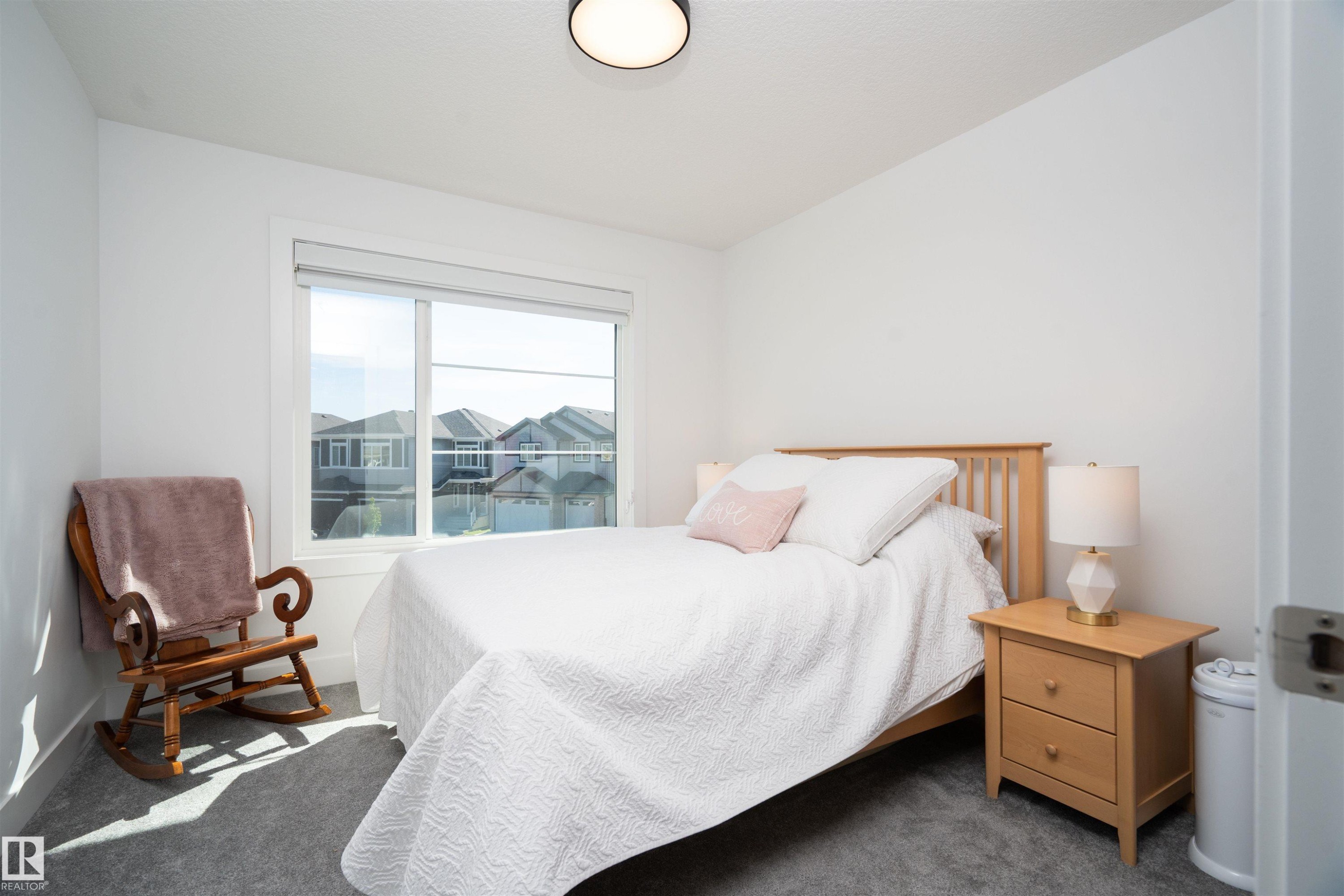 Bright bedroom featuring a large window, plush gray carpeting, white walls, a flush-mount ceiling light, and white trim - 4714 Charles Bay Bay, Edmonton, AB