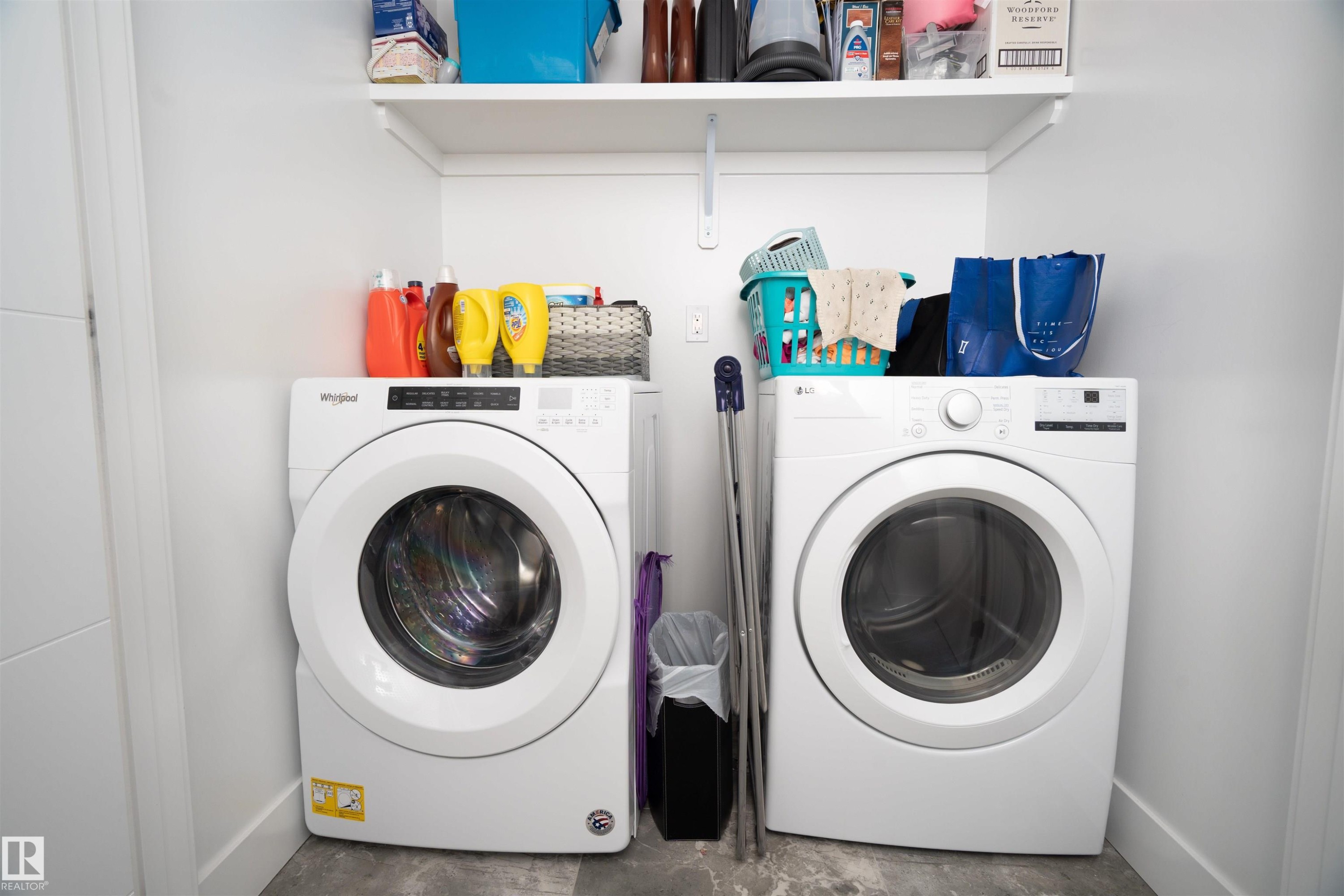 Dedicated laundry area featuring a white front-load washer and dryer, an overhead shelving unit, and a gray-toned floor - 4714 Charles Bay Bay, Edmonton, AB