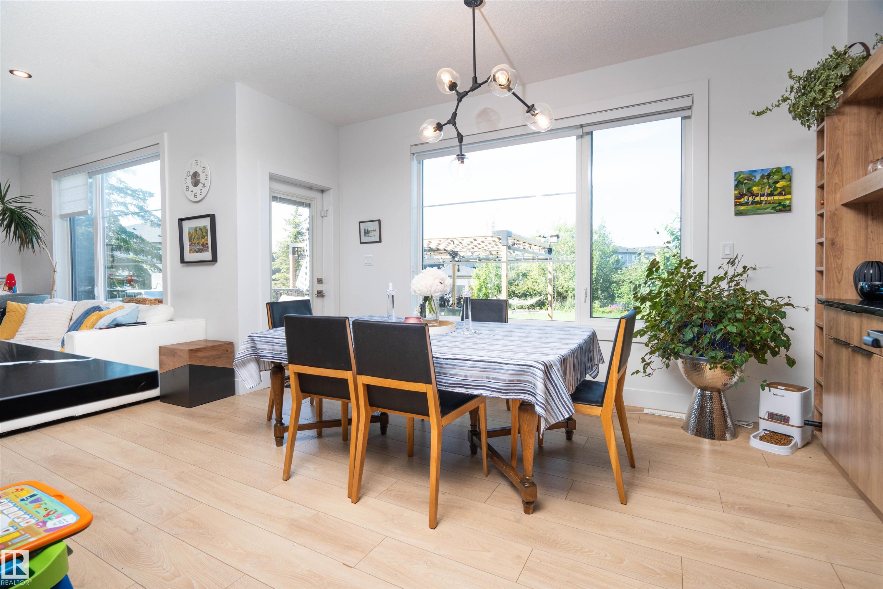Open-concept dining area featuring light wood-finish flooring, a contemporary black light fixture, and a large sliding glass door providing access to the exterior - 4714 Charles Bay Bay, Edmonton, AB