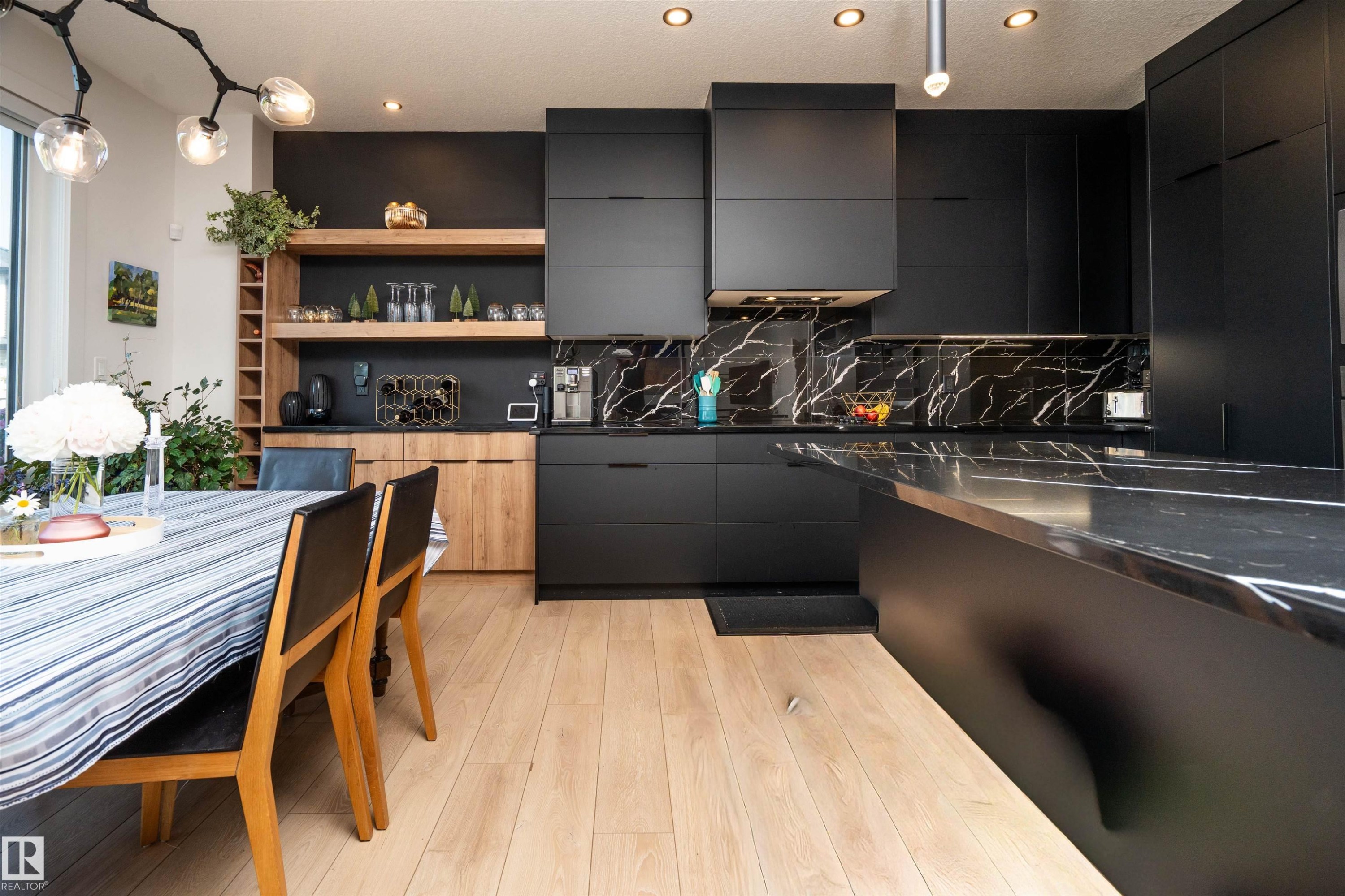 Contemporary kitchen featuring dark flat-panel cabinetry, a large island with a dark countertop, and light wood-finish flooring - 4714 Charles Bay Bay, Edmonton, AB