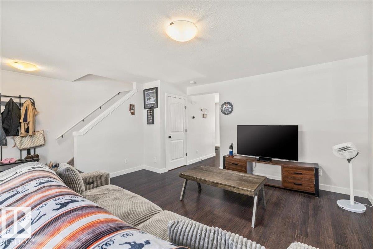 Spacious living area featuring dark wood-finish flooring, white walls, and a staircase with white risers and handrail - 125 Birchwood Close, Devon, AB