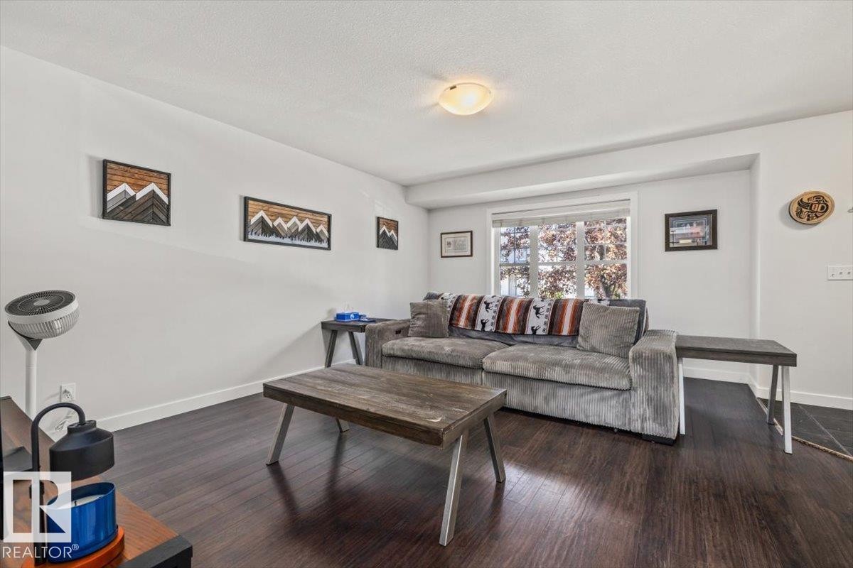 Spacious living area featuring dark wood-finish flooring, white baseboards, and a large window - 125 Birchwood Close, Devon, AB