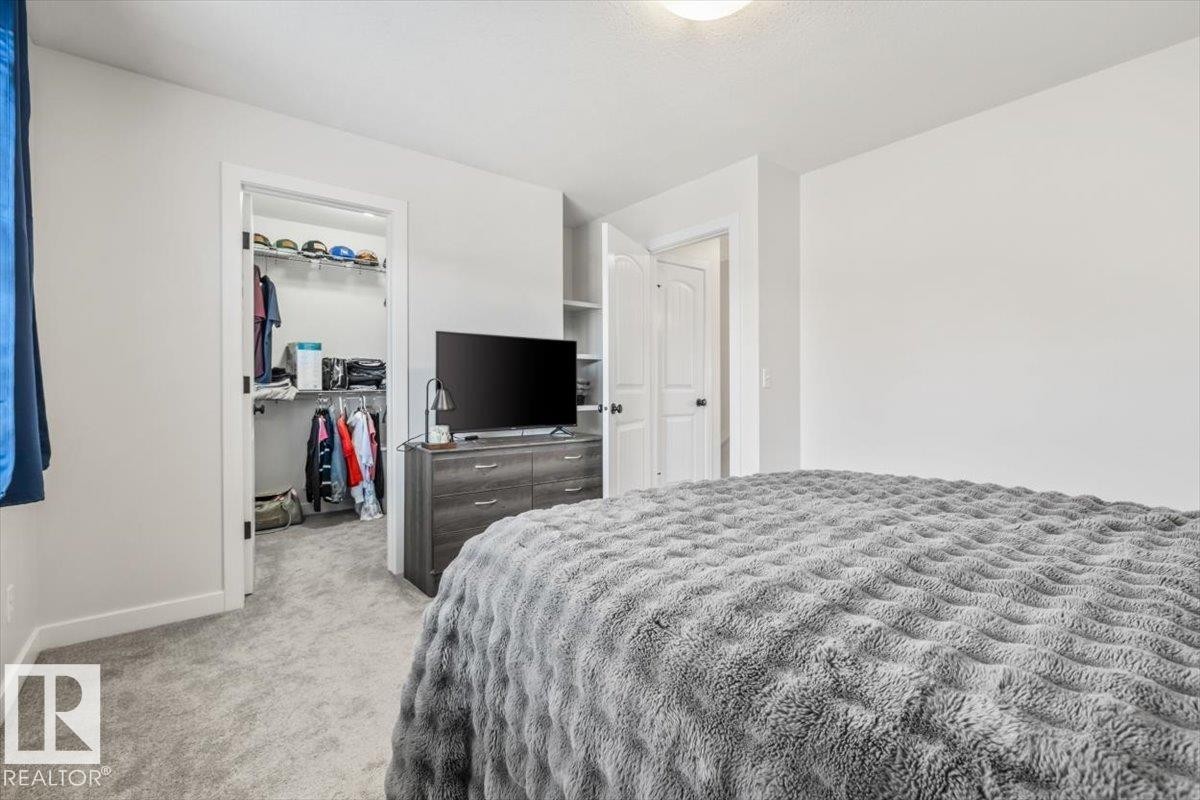 Carpeted interior space featuring a walk-in closet with built-in shelving, a dresser with storage, and a separate interior door - 125 Birchwood Close, Devon, AB