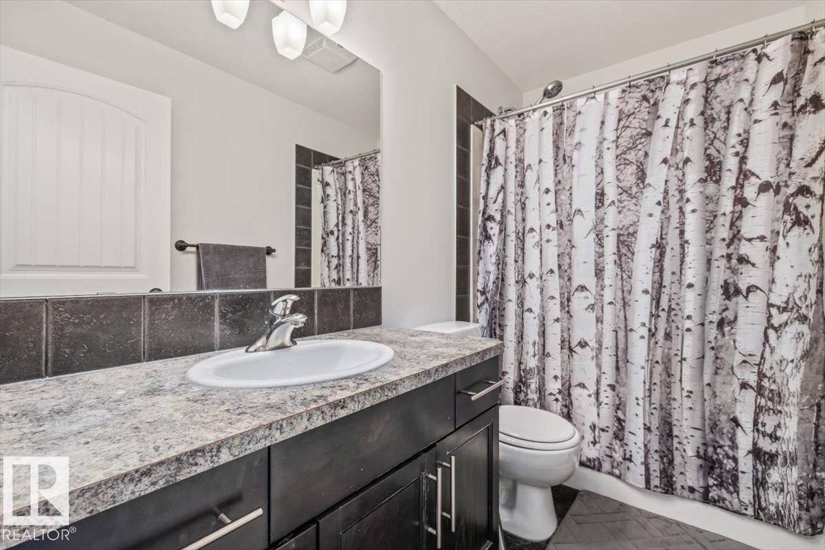 Bathroom featuring a light-colored countertop with an oval undermount sink, dark wood-finish cabinetry, a large mirror, and dark tile backsplash - 125 Birchwood Close, Devon, AB