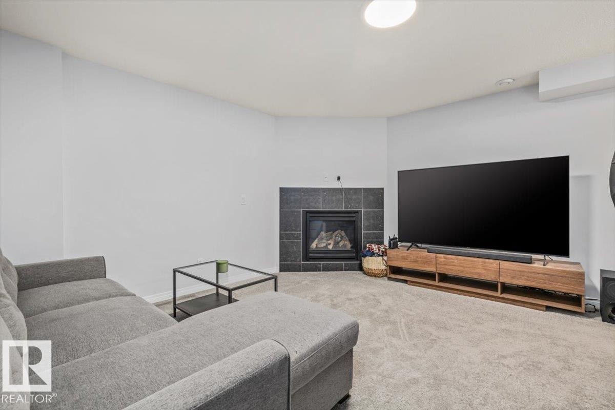Carpeted living area featuring a corner fireplace with dark tile surround, light-colored walls, and recessed lighting - 125 Birchwood Close, Devon, AB