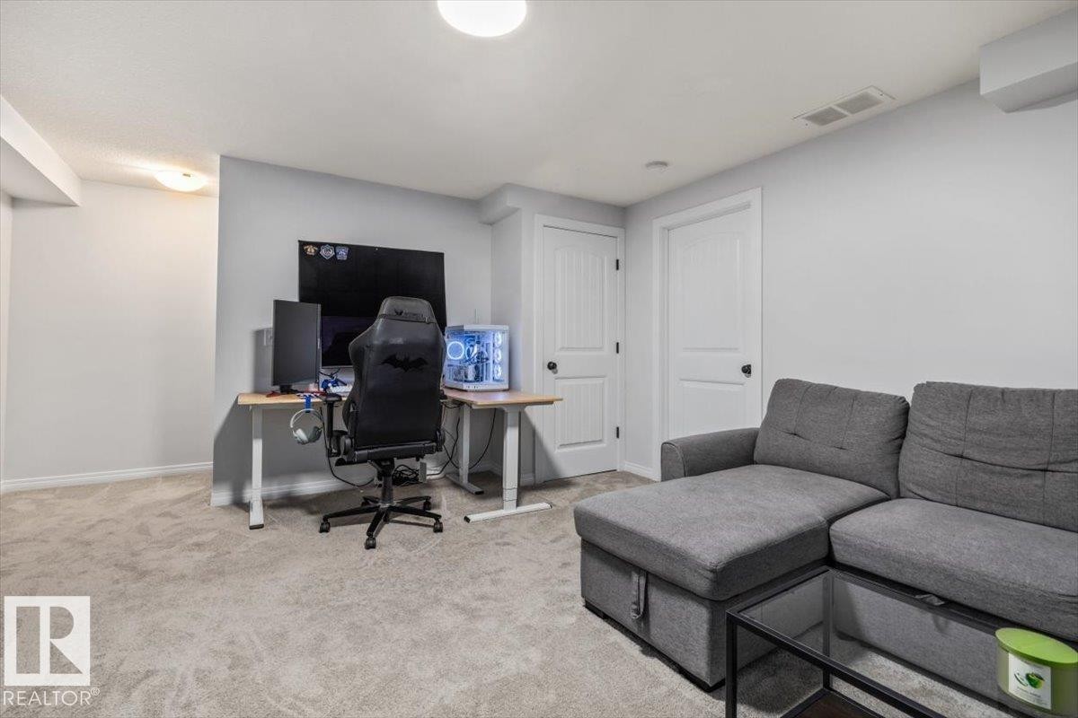 Spacious carpeted room featuring light gray walls, two paneled doors with black hardware, and an overhead flush-mount light fixture - 125 Birchwood Close, Devon, AB